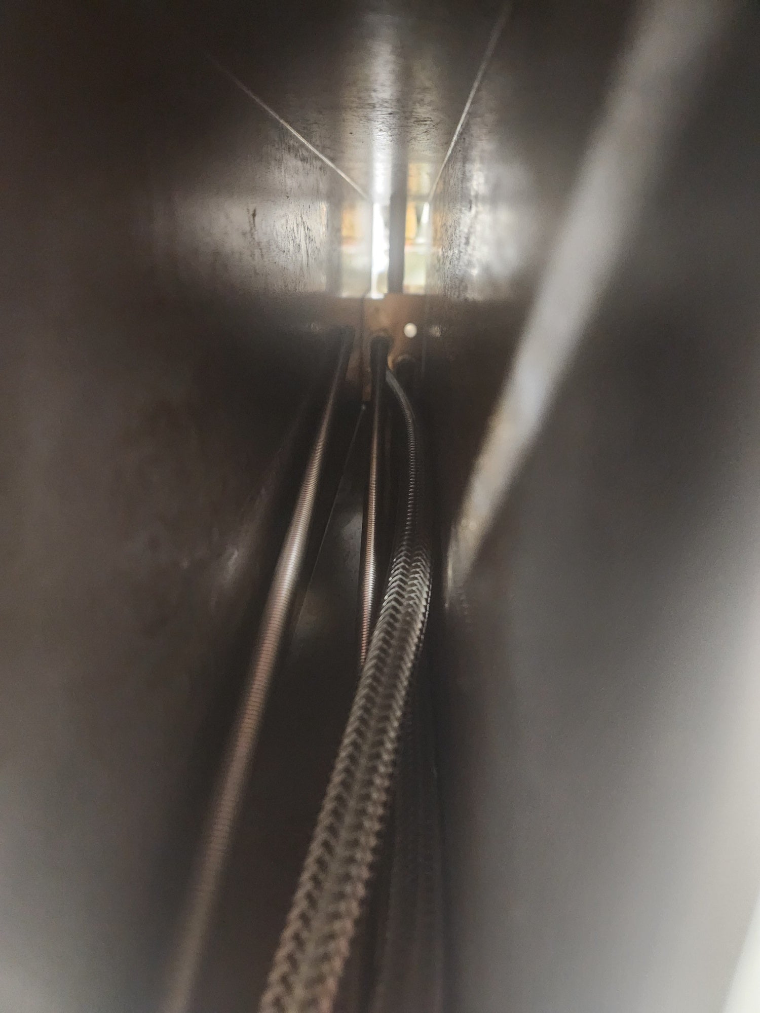 A close-up view inside a dark metallic cylindrical chamber, showing a braided metal cable running down the center toward a bright opening at the top.