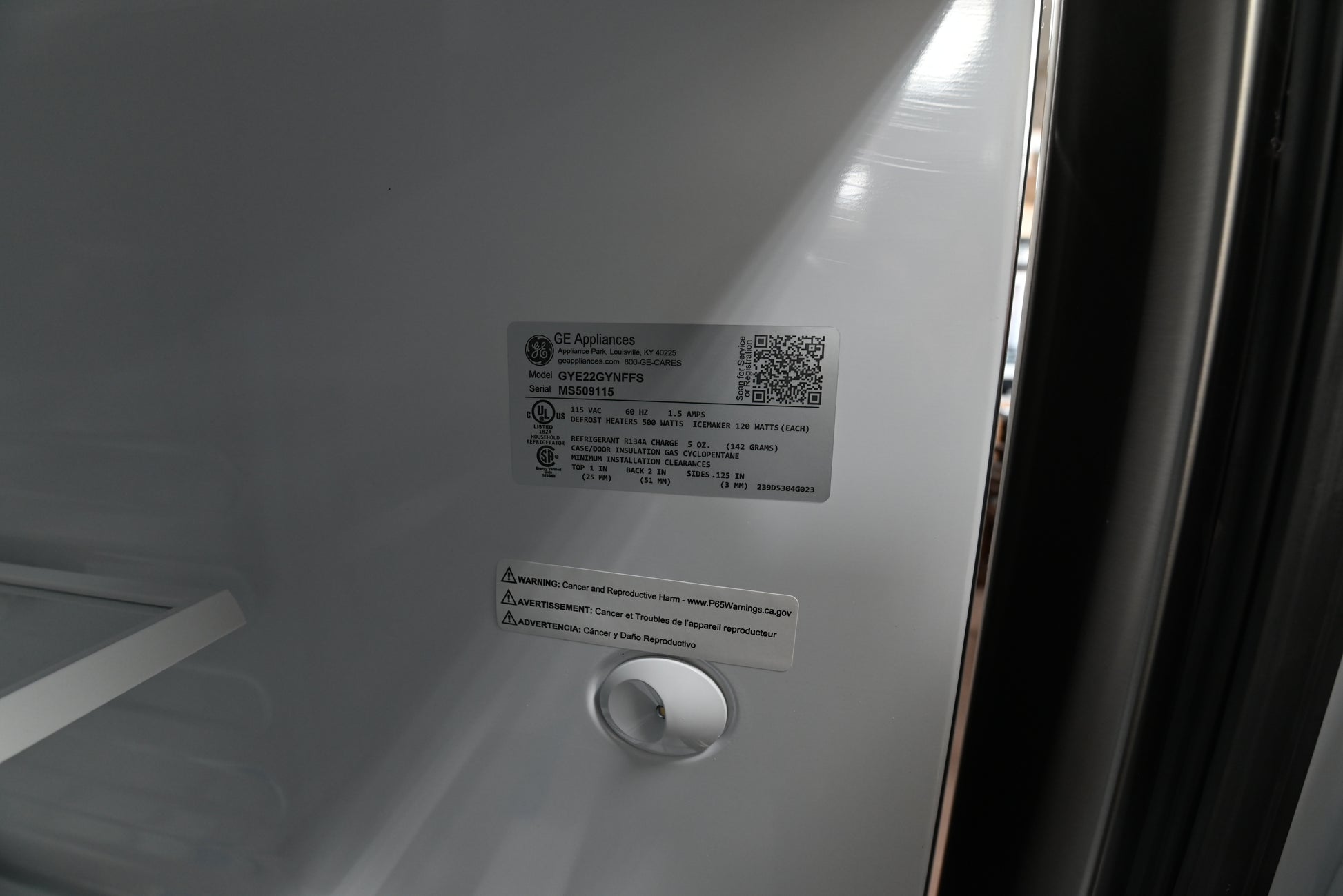 Close-up of the inside of a white refrigerator door showing product labels and a circular opening near the bottom.