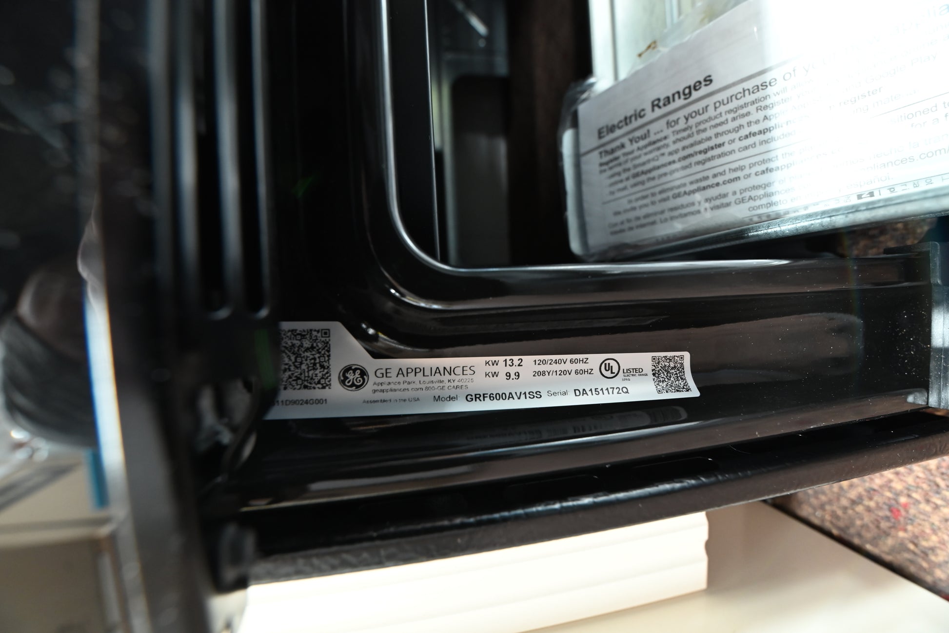 Close-up of a GE Appliances appliance interior showing a black frame, a product label with QR codes, and part of the white instruction booklet inside.