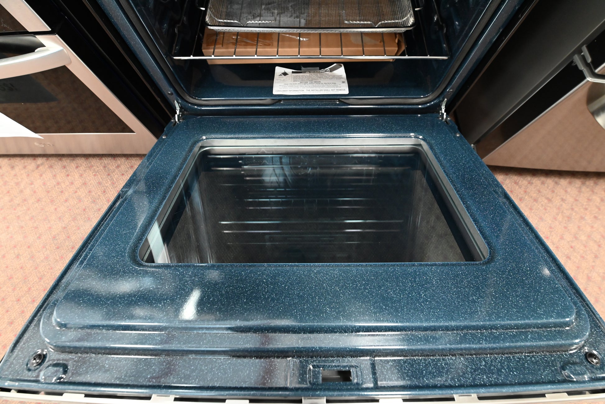 An open dark blue speckled gas range oven door showing the interior cavity, glass window, and upper rack.