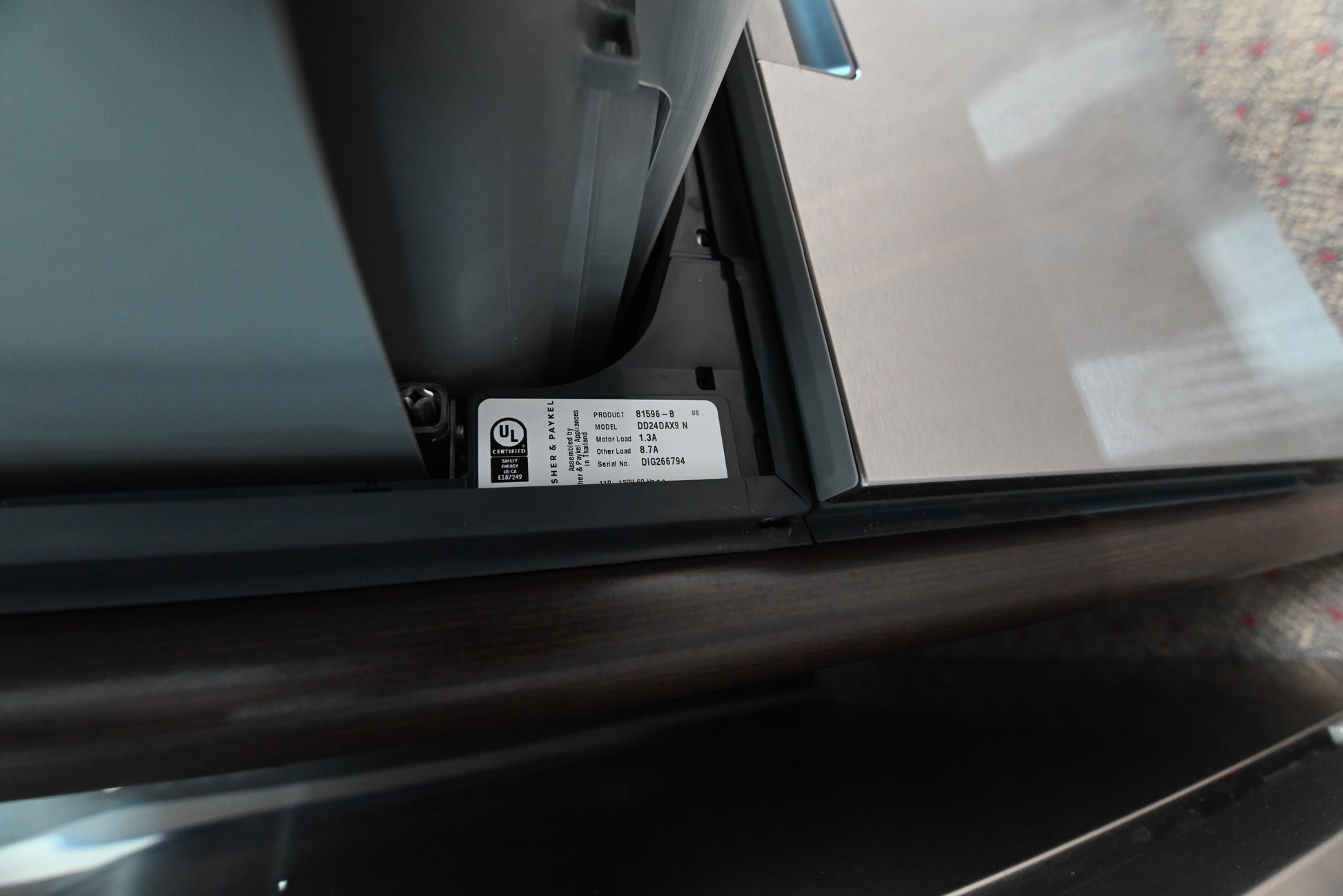 Close-up of the lower edge of a dark gray appliance, showing a white UL certification label attached to the black trim.