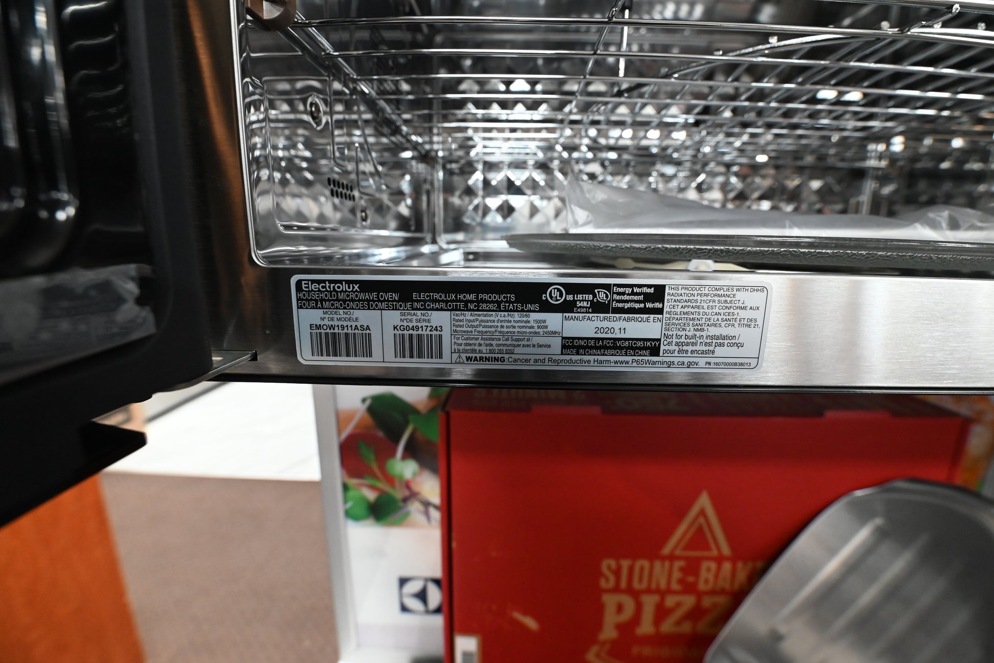 Close-up of the interior stainless steel door and control panel of an Electrite countertop oven, with a product label visible and a red Stone-Baked Pizza box below.