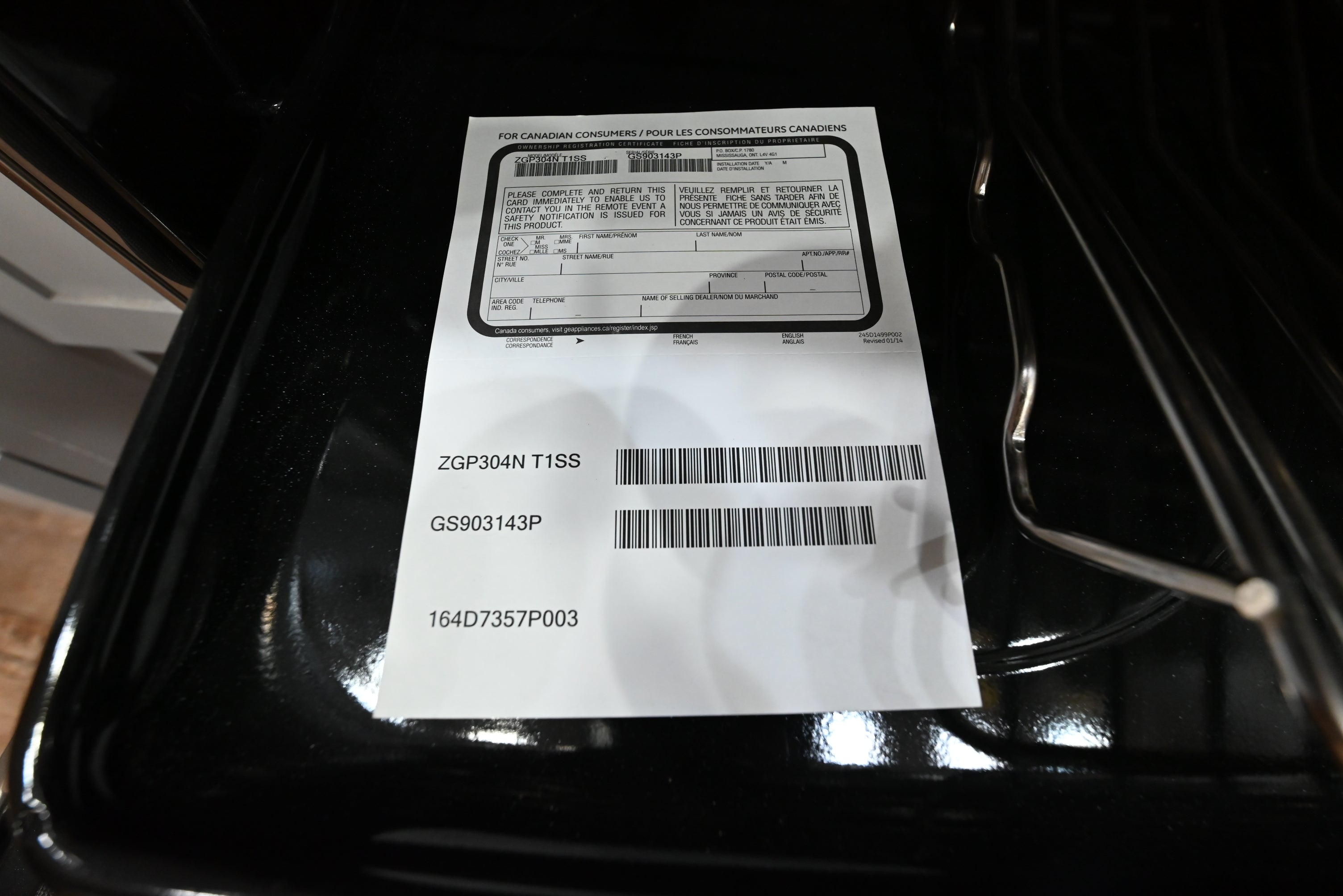 A white paper label with printed barcodes and text placed on the inside of a black oven or cooktop.