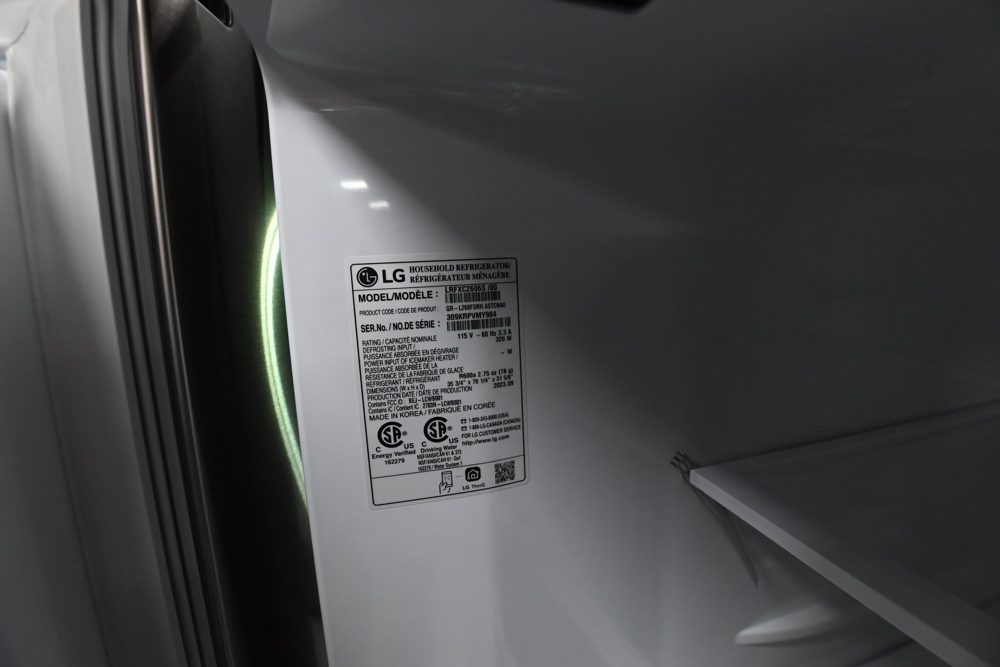 An interior close-up of a white appliance, likely a refrigerator or freezer door and shelf area, showing an LG model label sticker with regulatory text.
