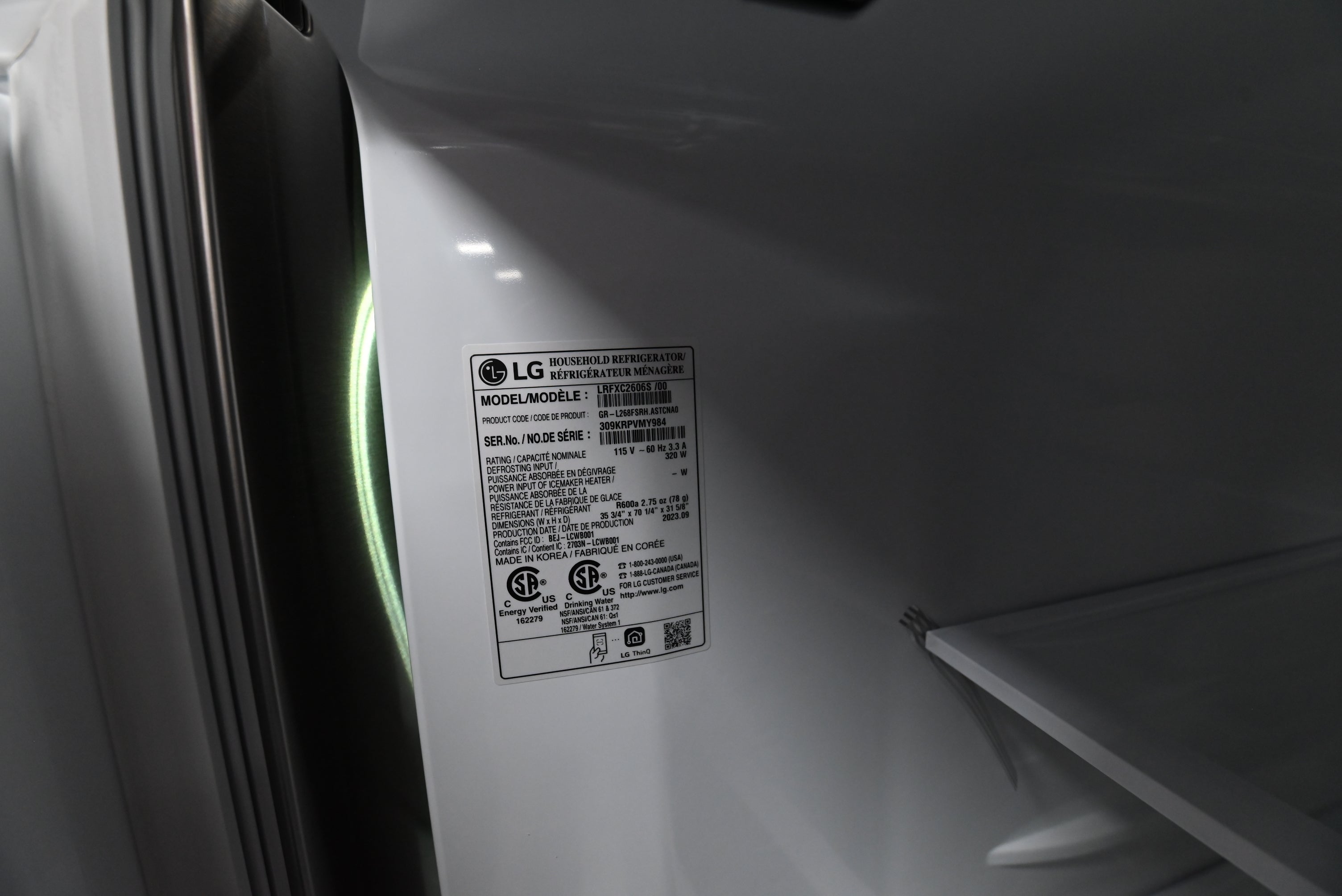 An interior close-up of a white appliance, likely a refrigerator or freezer door and shelf area, showing an LG model label sticker with regulatory text.