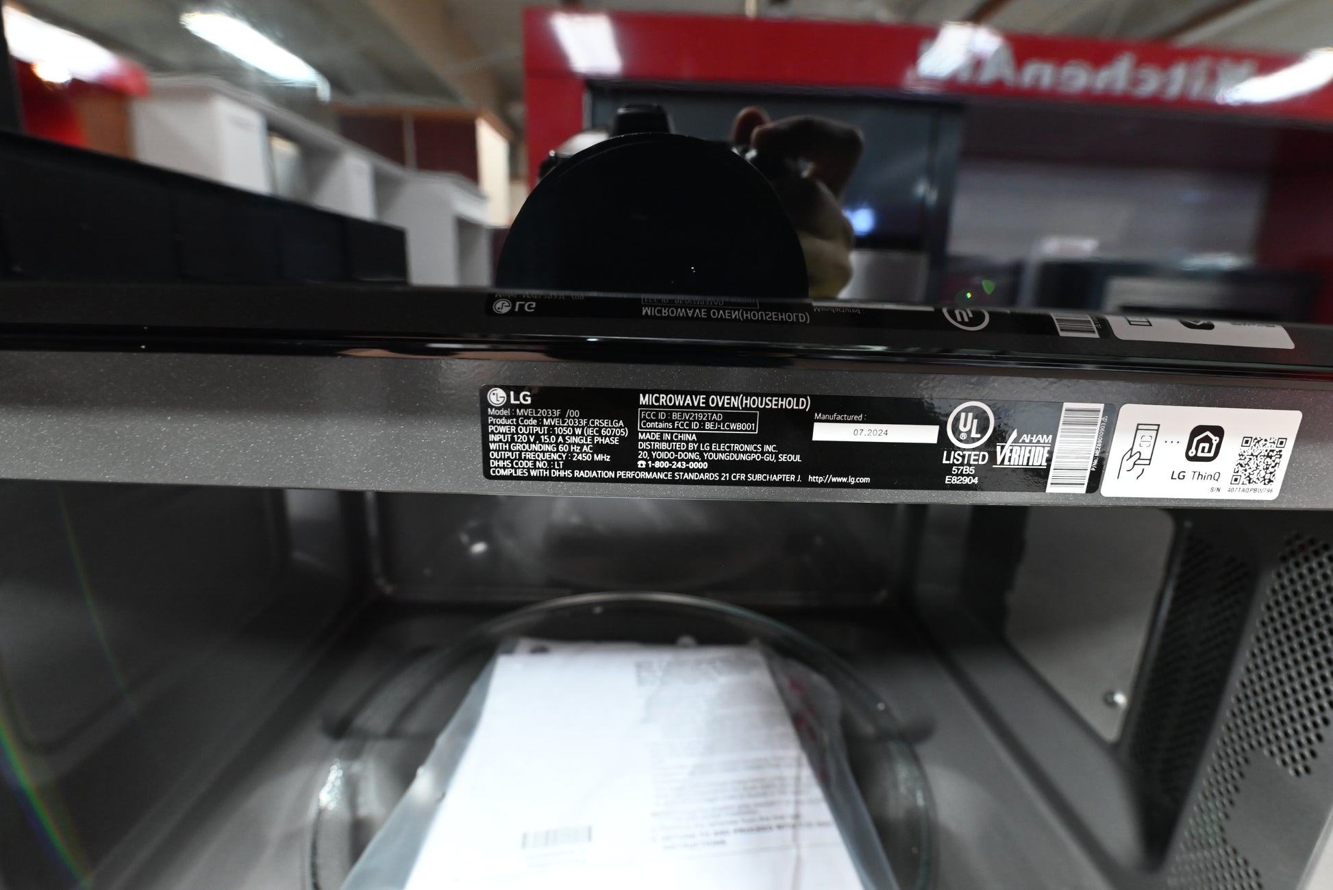 Close-up of the interior top panel of an LG microwave oven, showing the black control panel edge, product labels, and the inside of the dark gray cavity.