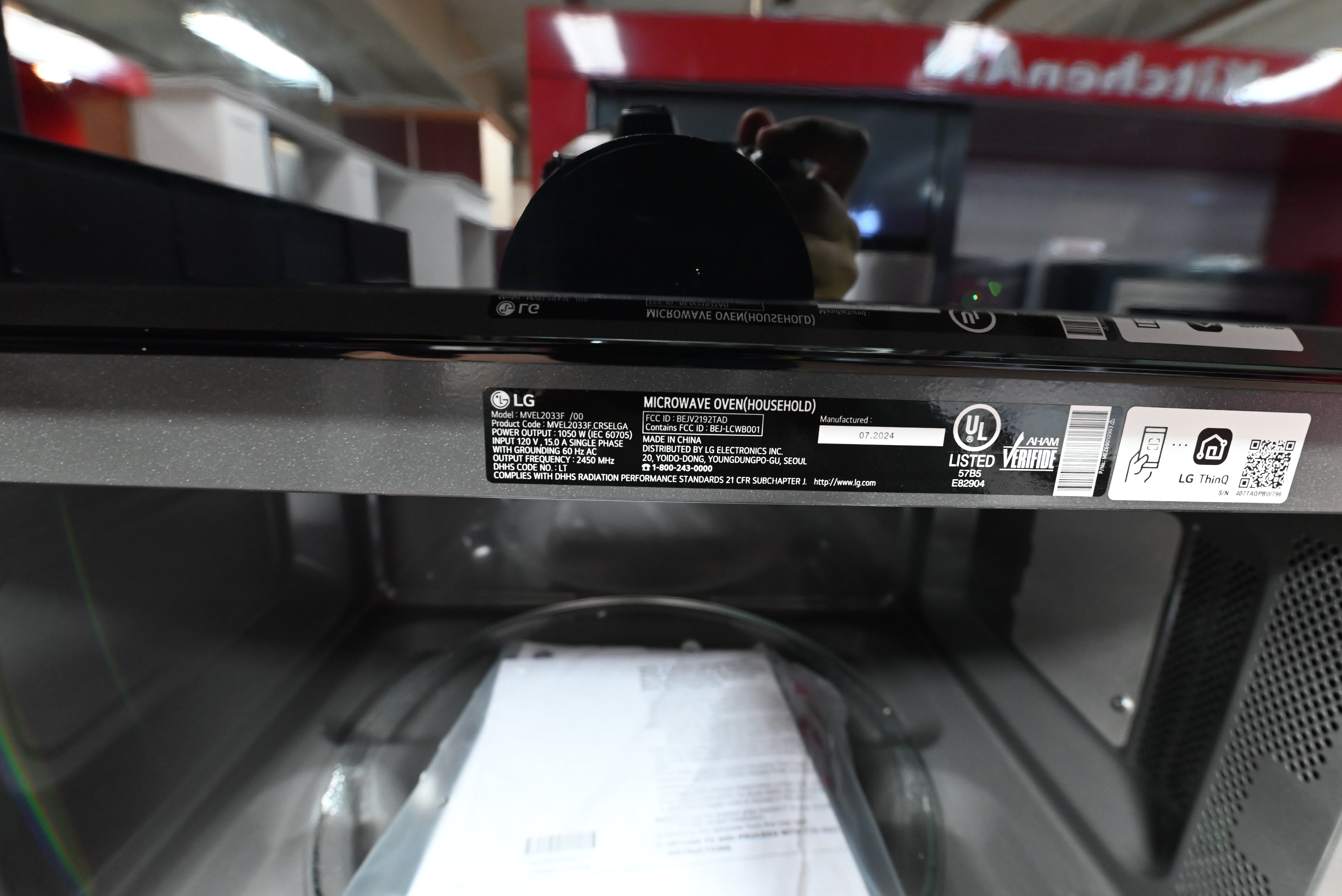 Close-up of the interior top panel of an LG microwave oven, showing the black control panel edge, product labels, and the inside of the dark gray cavity.
