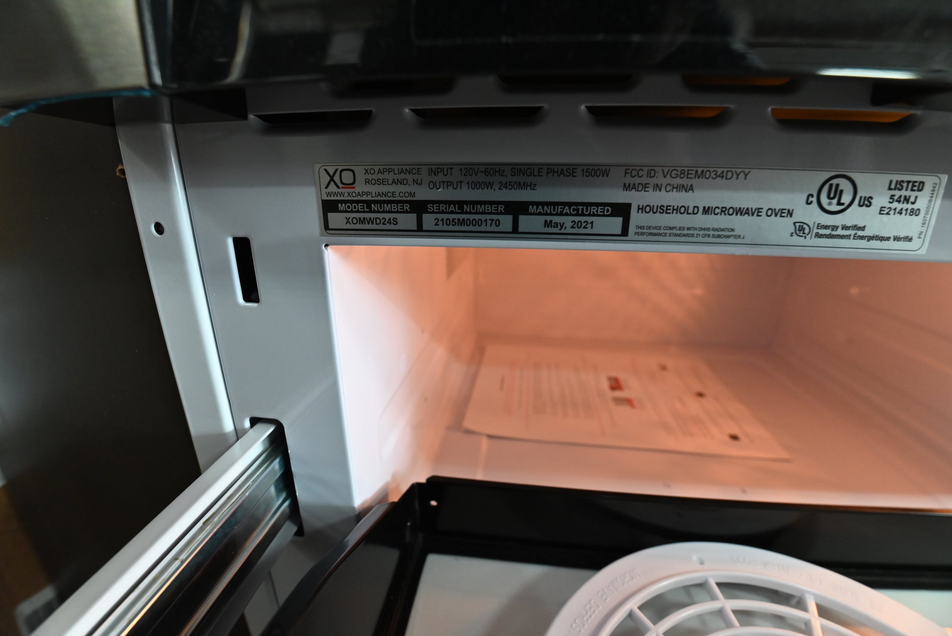 Open stainless steel microwave oven showing the interior light on, with a paper label containing model and certification information on the inside wall.