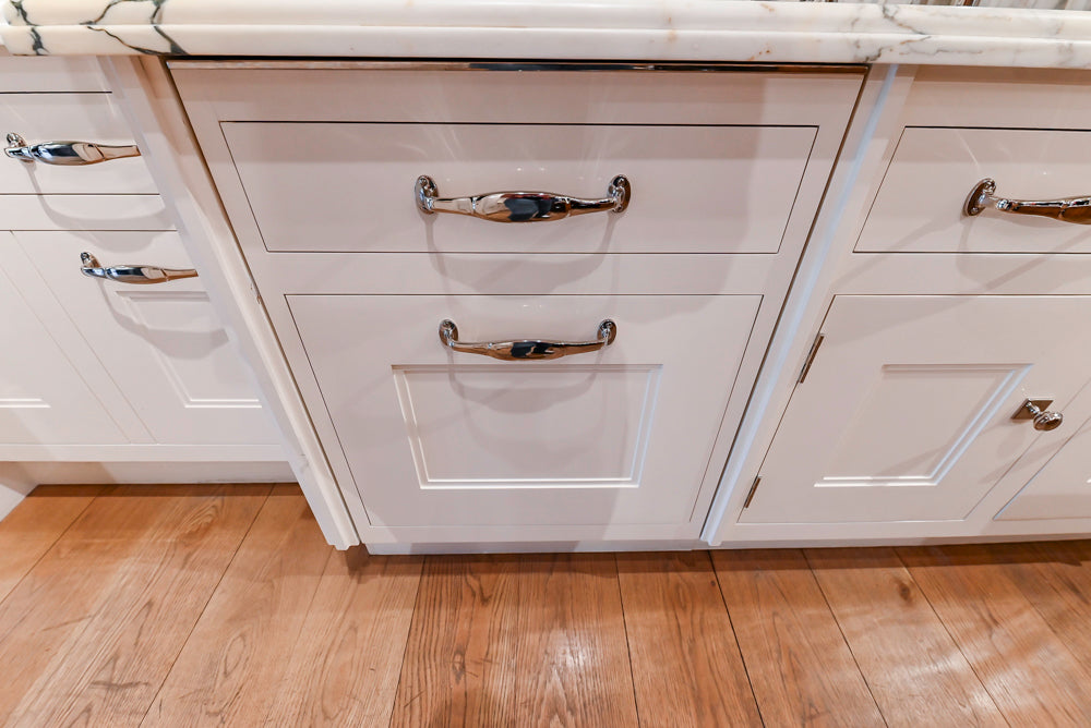 Close-up of white kitchen cabinets with silver handles on a wooden floor.