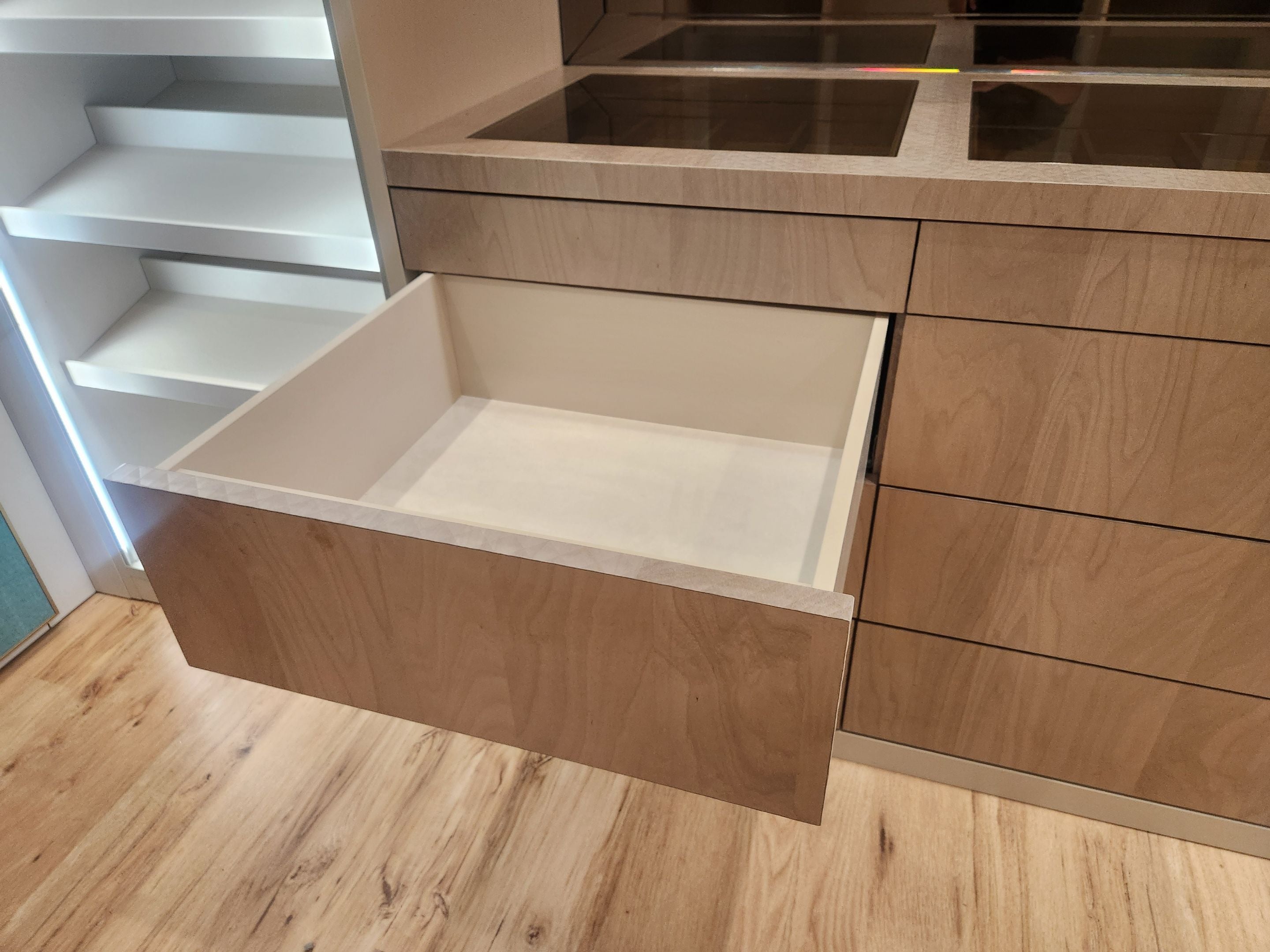 A light oak wood drawer with a cream-colored interior pull-out drawer, shown in a modern kitchen setting with matching wood cabinetry and a light wood floor.