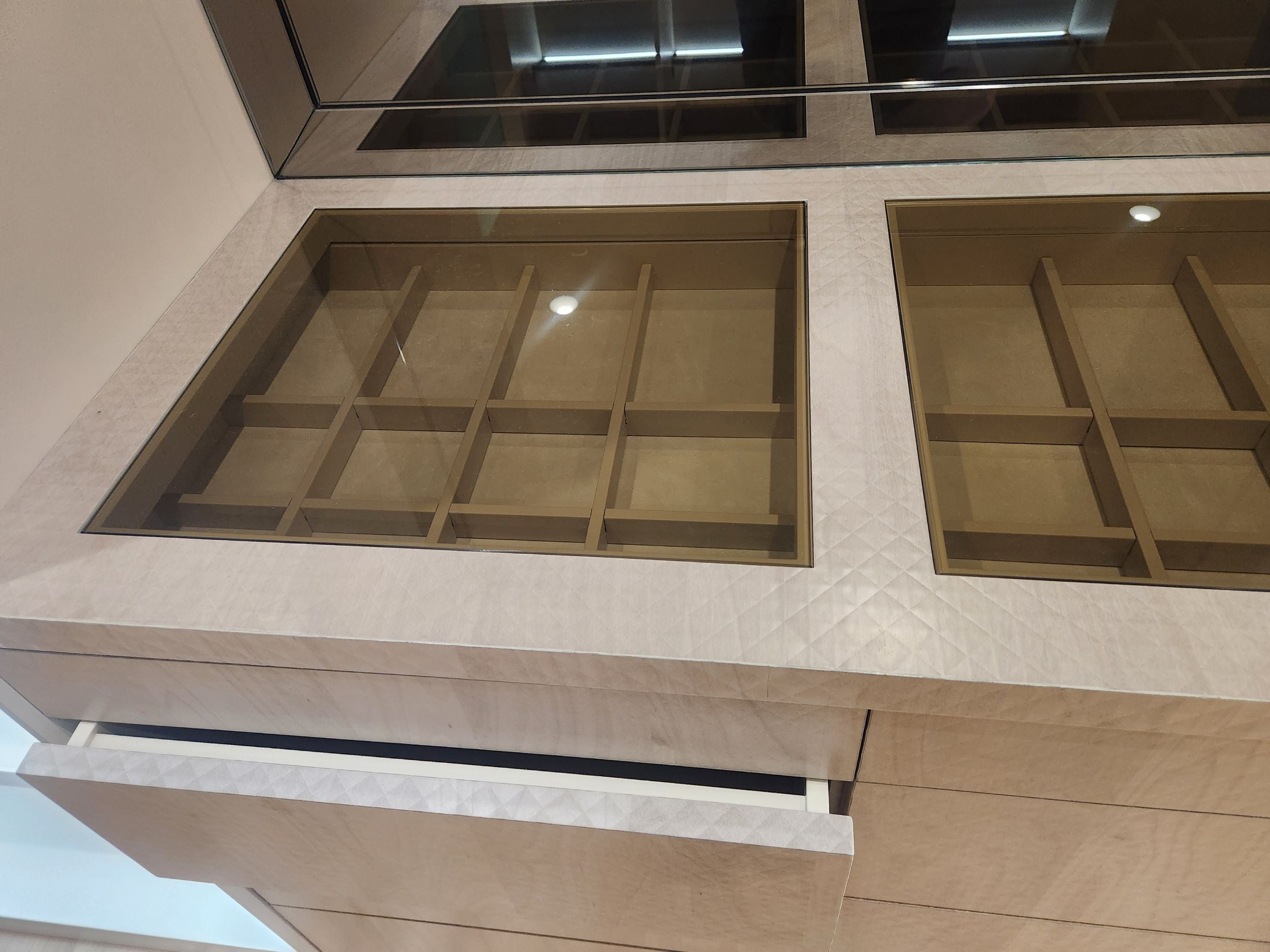 A close-up of a modern vanity or cabinet interior with two rectangular recessed display compartments framed in dark metal, set into a light beige stone or wood cabinet front.