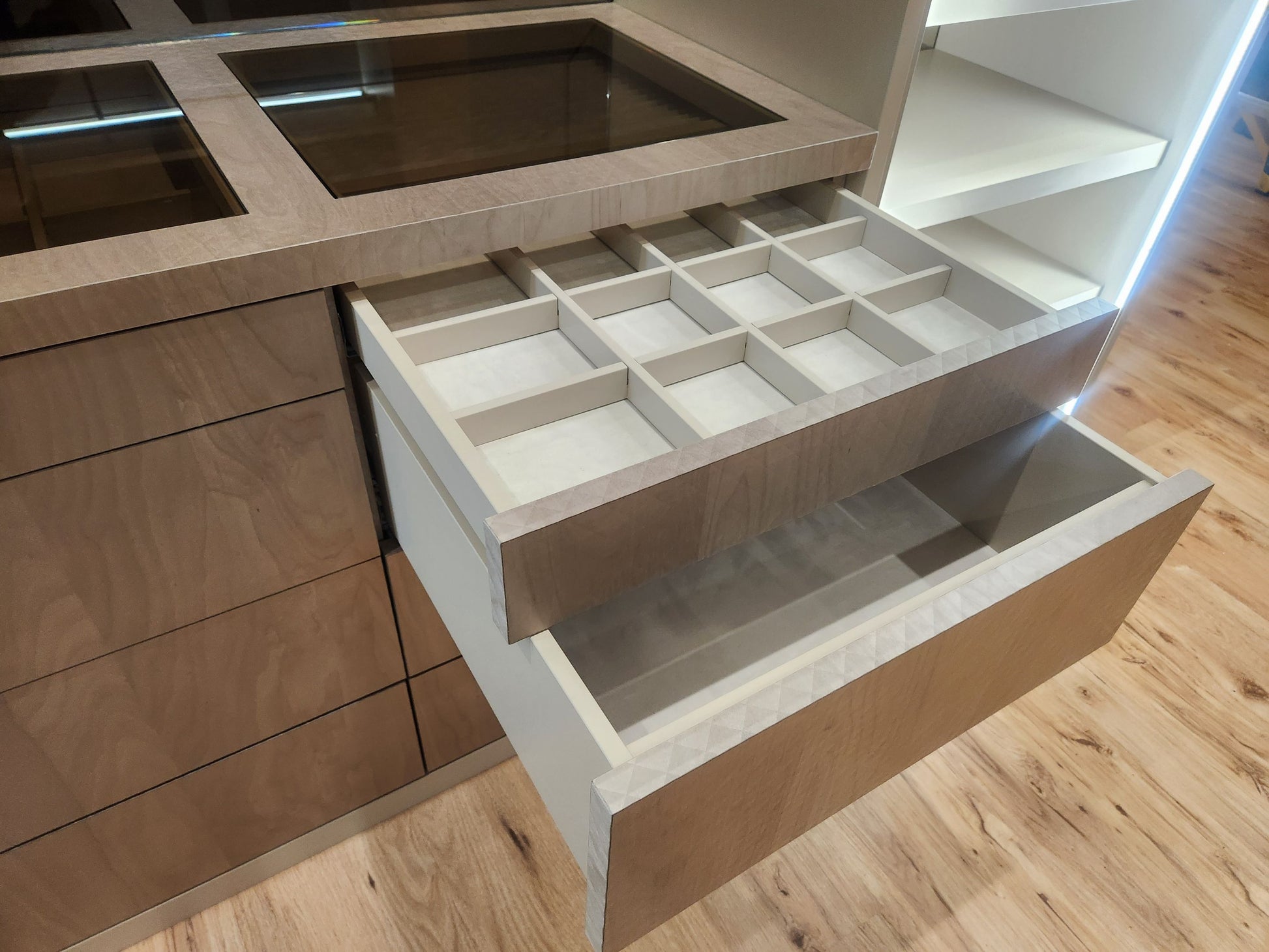 A close-up of a modern kitchen cabinet with two open drawers. The upper drawer is fitted with a light beige compartment organizer tray, while the lower drawer is empty.
