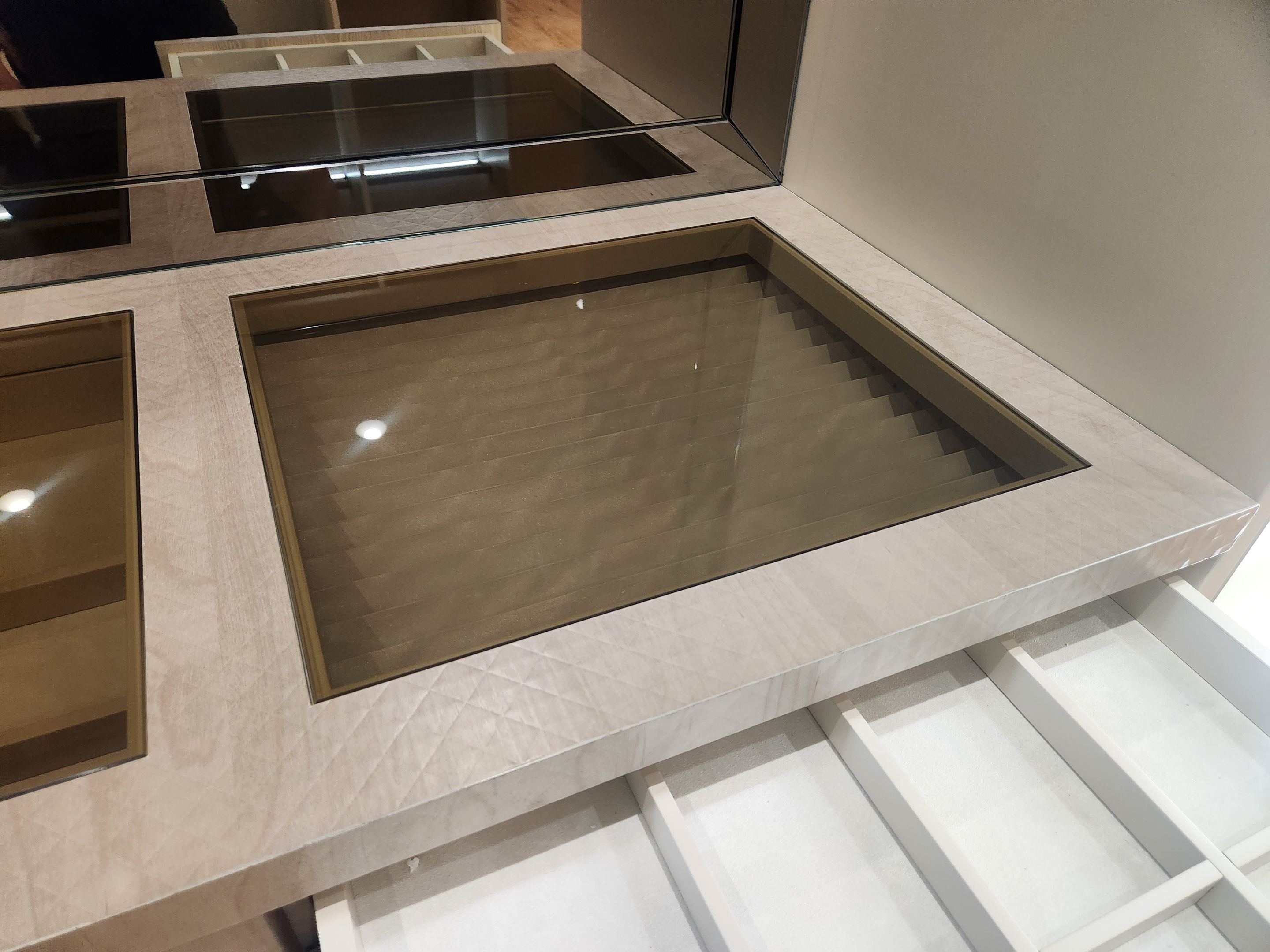A close-up of a modern vanity or cabinet interior with a rectangular recessed mirror or glass panel set into a light beige stone surround, above white storage compartments.
