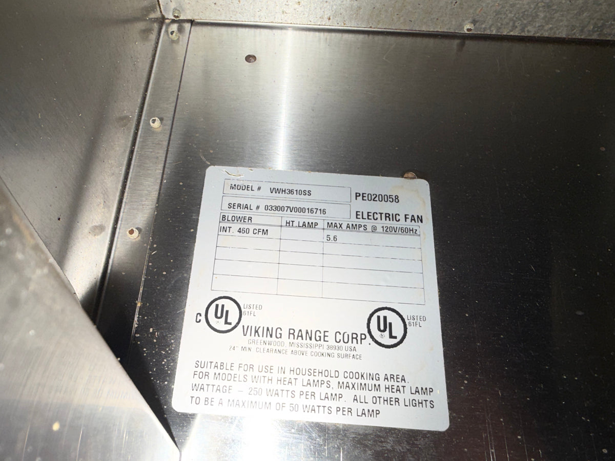 A close-up of a metal appliance interior showing a white product information label with printed text and UL logos. The label includes Viking Range Corp branding and model details for an electric fan.