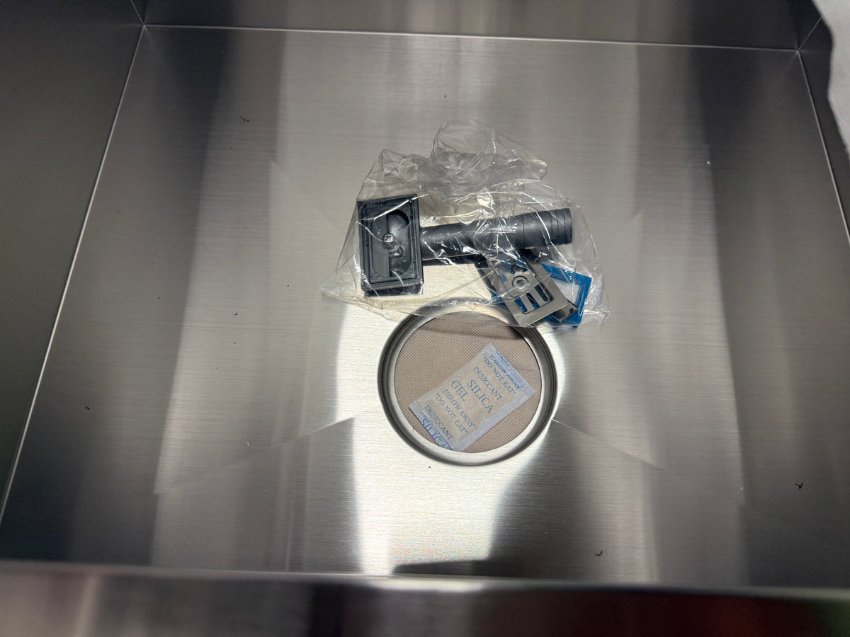 A stainless steel appliance interior with a circular opening and a small packaged hardware component resting inside next to the opening.