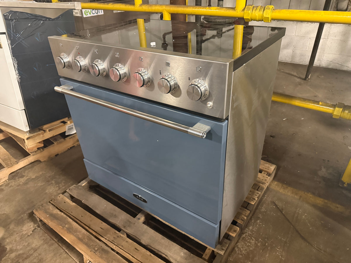 A built-in gas range stove with a slate blue oven door and stainless steel control panel, sitting on a wooden pallet in a warehouse setting.