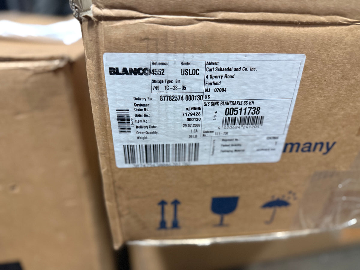 A close-up of a brown cardboard shipping box with a white printed label. The label shows the brand name BLANCO and shipping details, with other shipping symbols printed on the cardboard below.