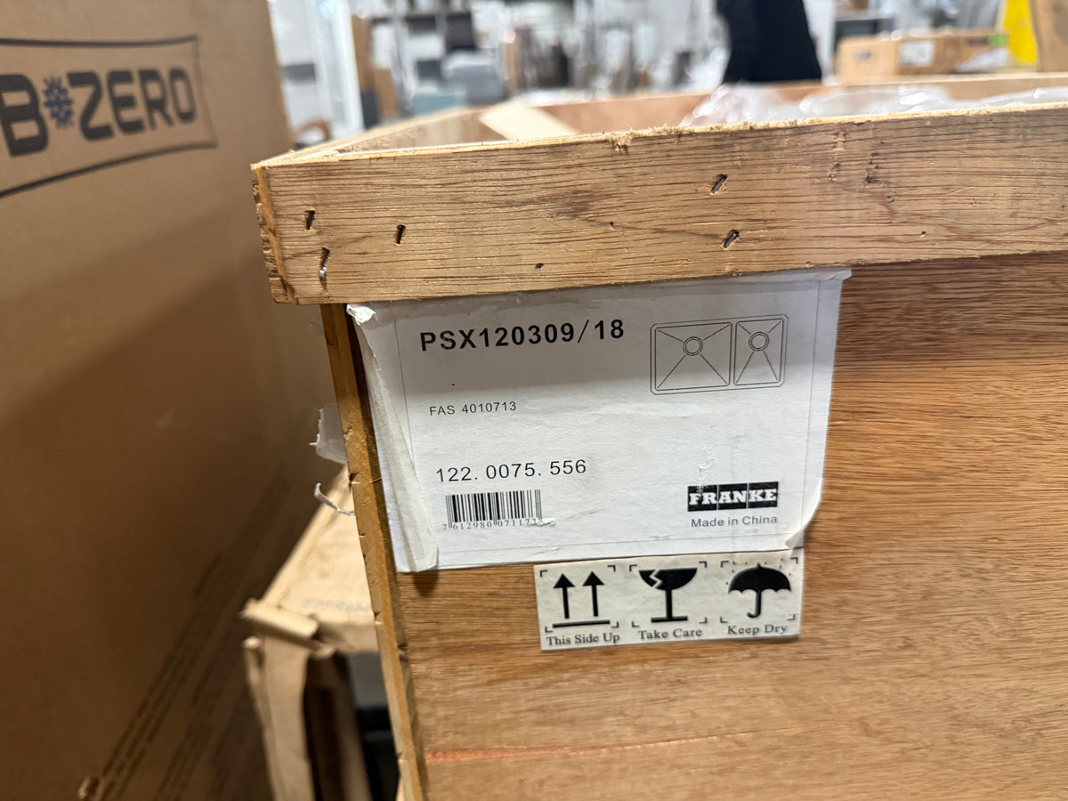 A close-up of a wooden shipping crate with a white paper label from Franke. The label shows the product code PSX120309/18, a barcode, and handling icons.