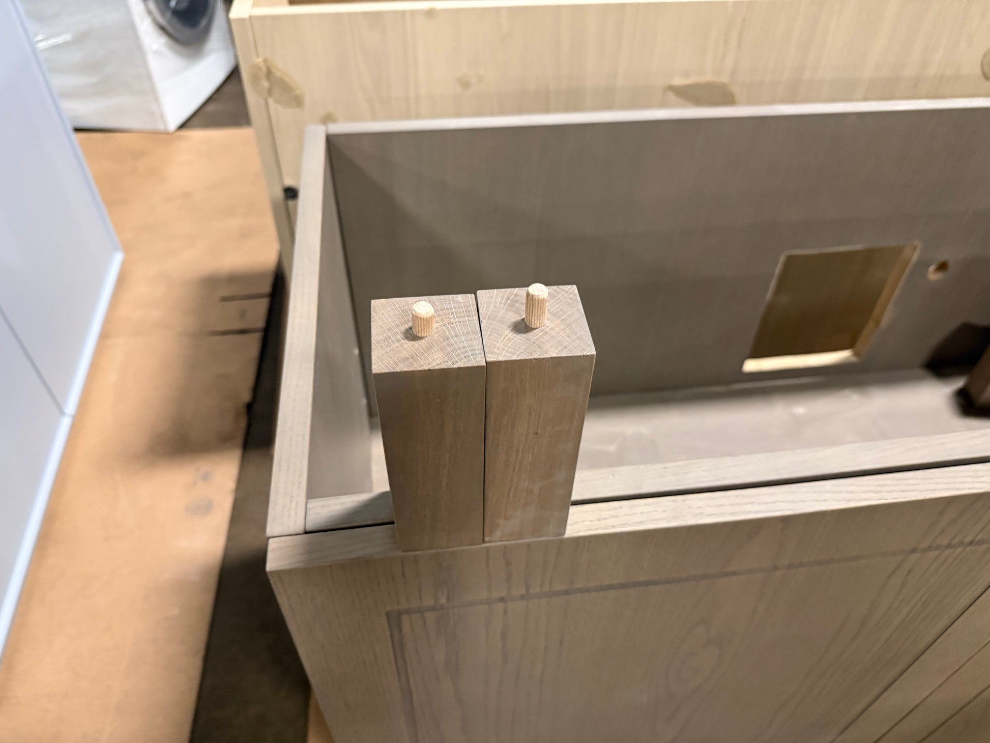 Close-up of a light wood cabinet or drawer front with two vertical wood blocks showing round pegs, set inside a larger matching wood structure.