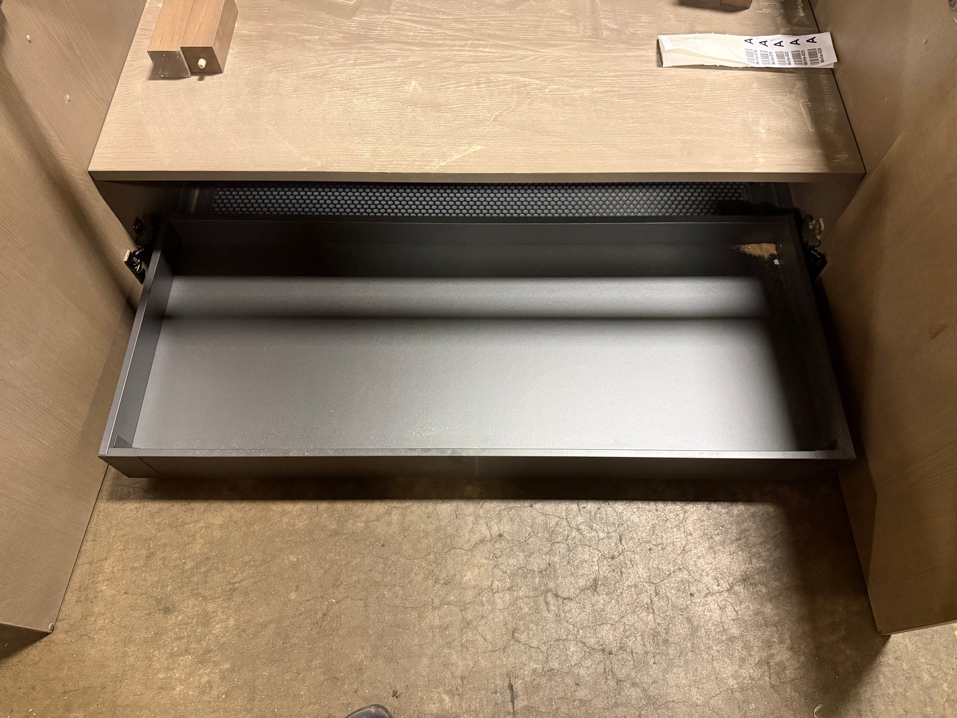 A dark gray metal drawer pull handle shown installed inside a light wood cabinet drawer, pulled open to reveal the interior.