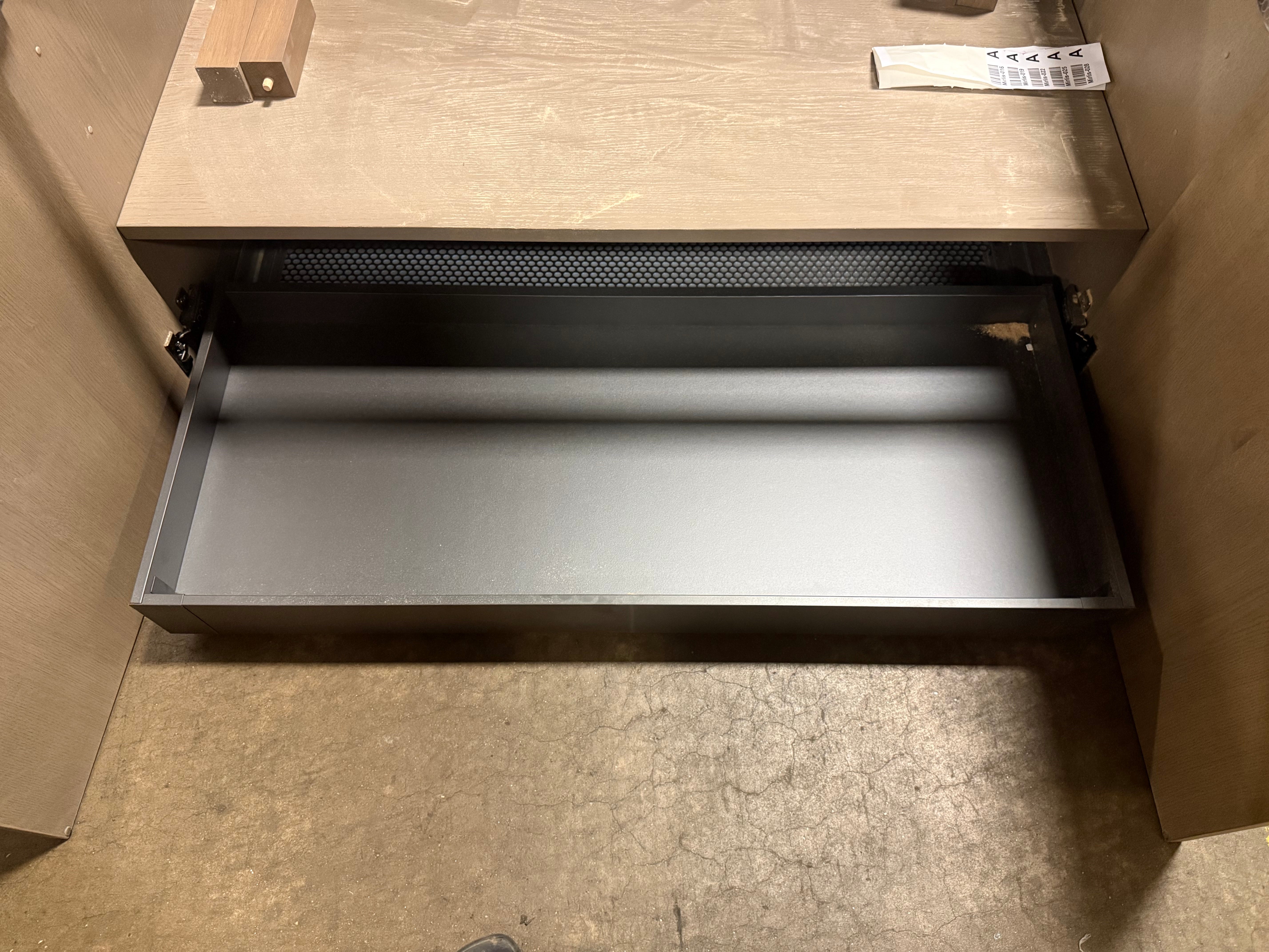 A dark gray metal drawer pull handle shown installed inside a light wood cabinet drawer, pulled open to reveal the interior.