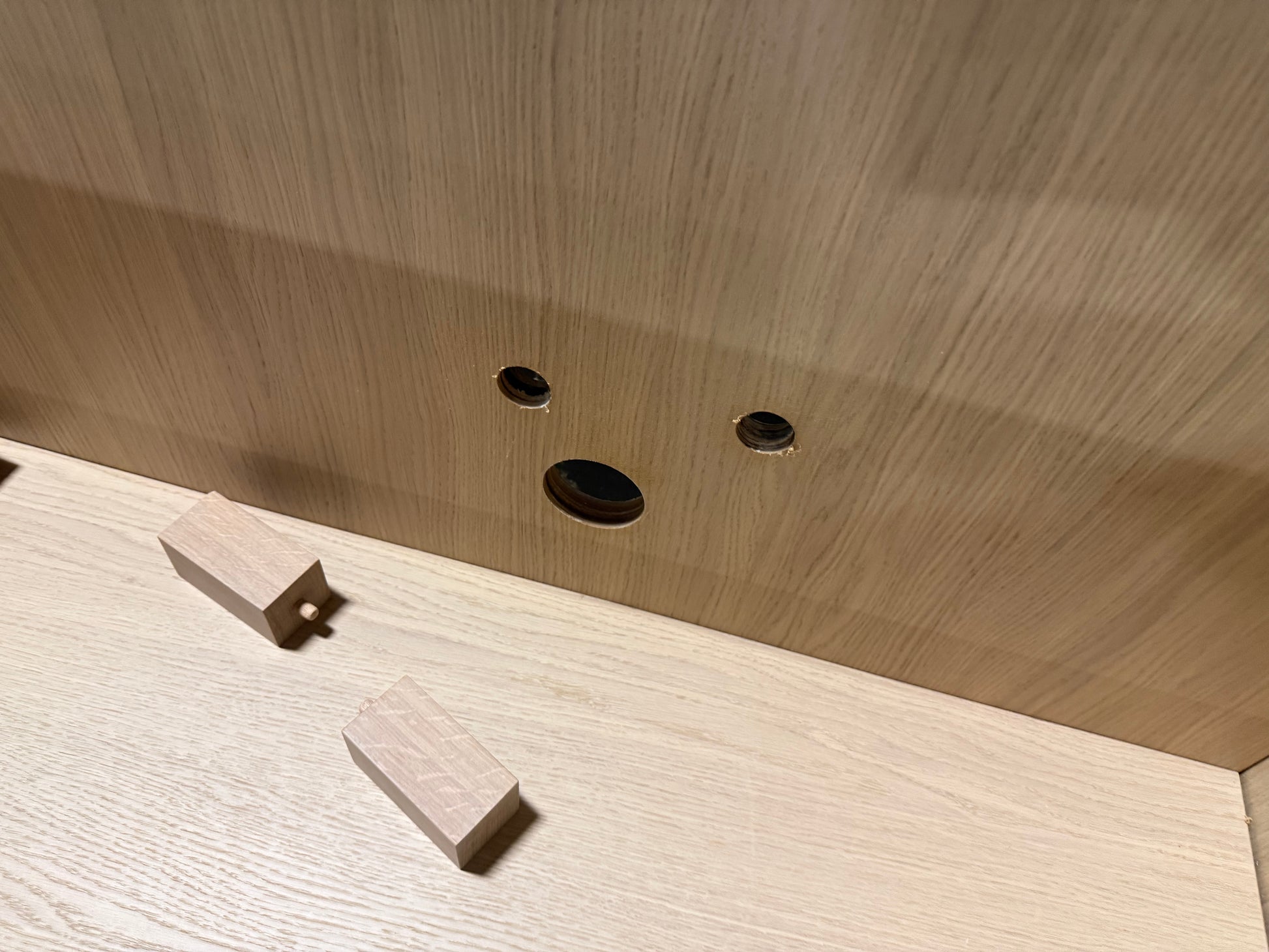 Close-up of a light wood cabinet interior showing a tongue-and-groove joint, pre-drilled holes, and two small wooden blocks on the shelf.