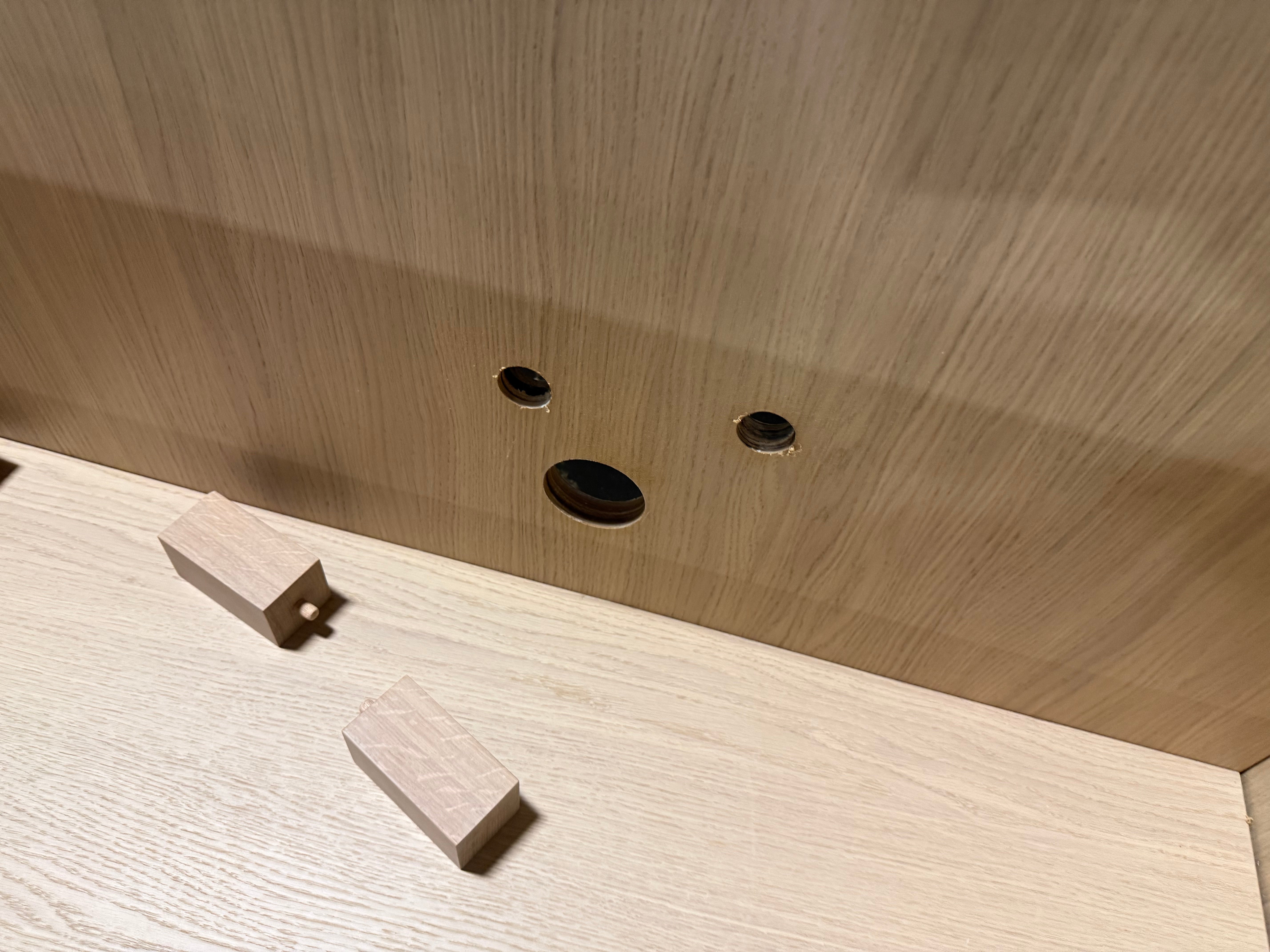 Close-up of a light wood cabinet interior showing a tongue-and-groove joint, pre-drilled holes, and two small wooden blocks on the shelf.