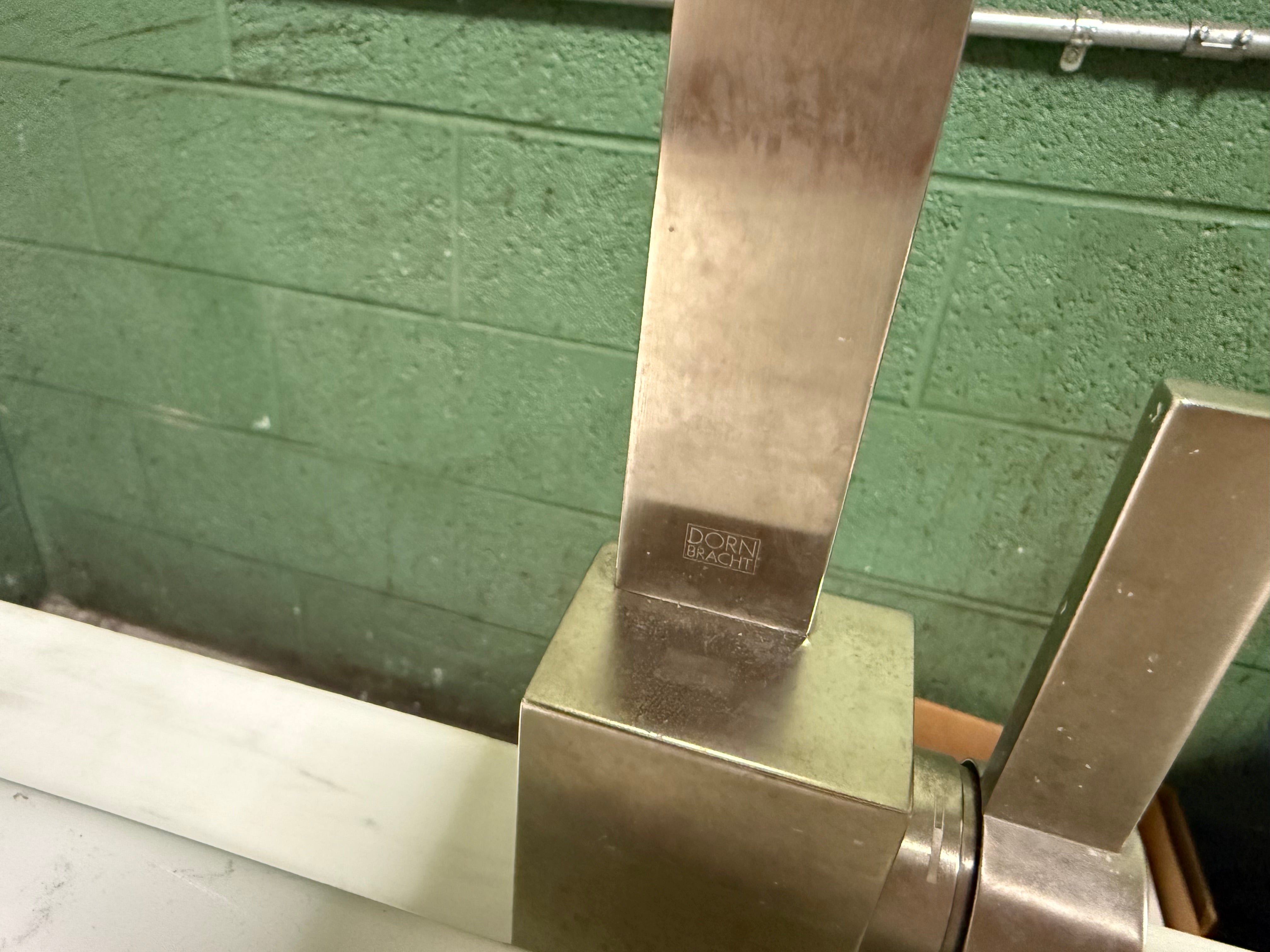 Close-up of a brushed stainless steel faucet handle on a white sink countertop against a green painted cinderblock wall.