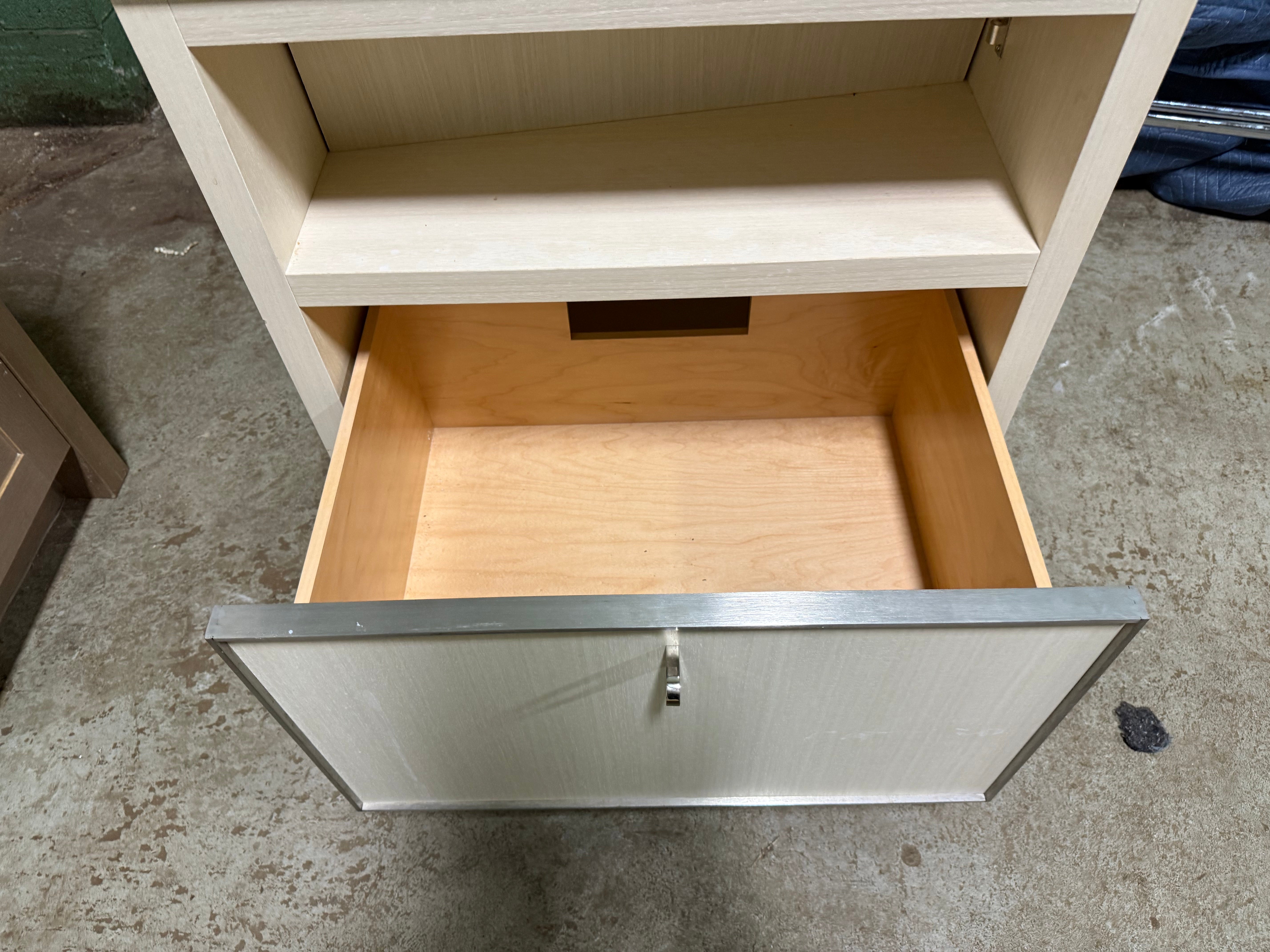 A light wood drawer cabinet with an open bottom drawer and an open upper shelf, photographed on a concrete floor.