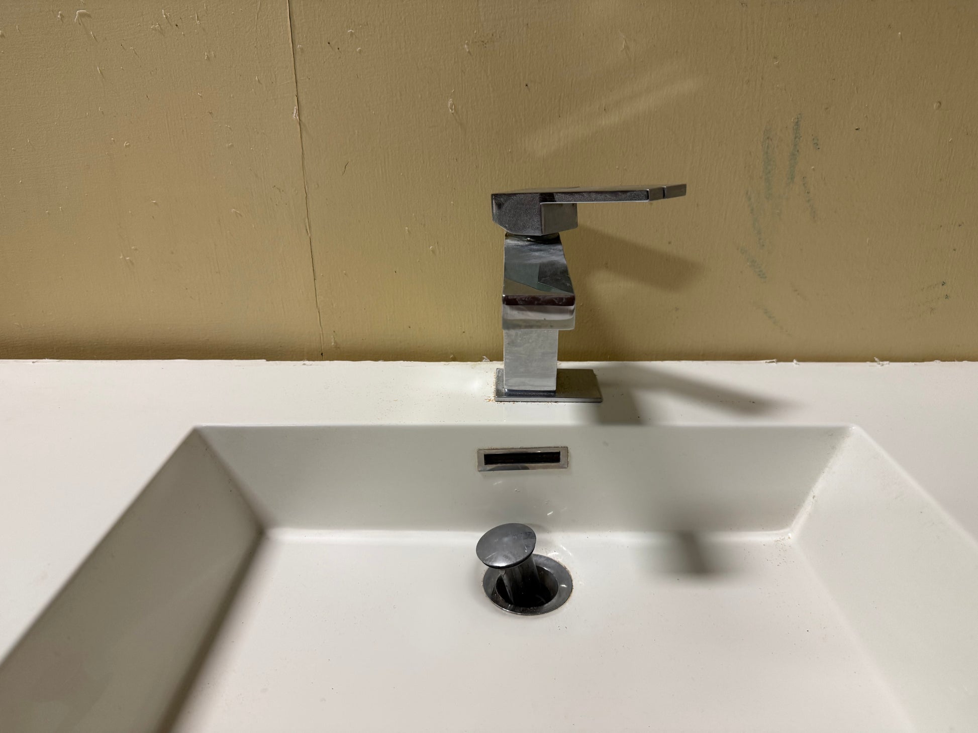 A modern chrome single-handle bathroom faucet mounted on a white sink basin against a beige wall.