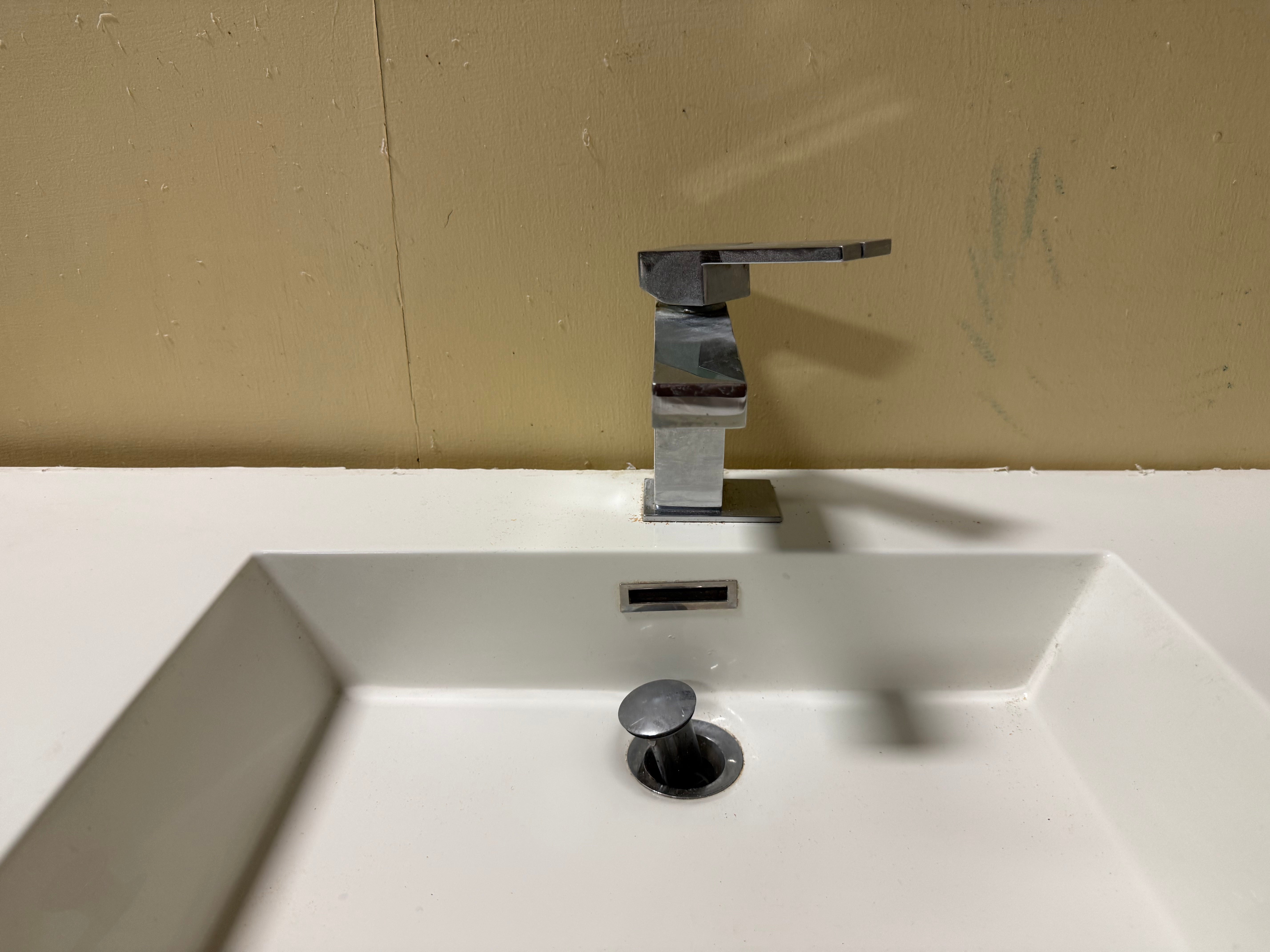 A modern chrome single-handle bathroom faucet mounted on a white sink basin against a beige wall.