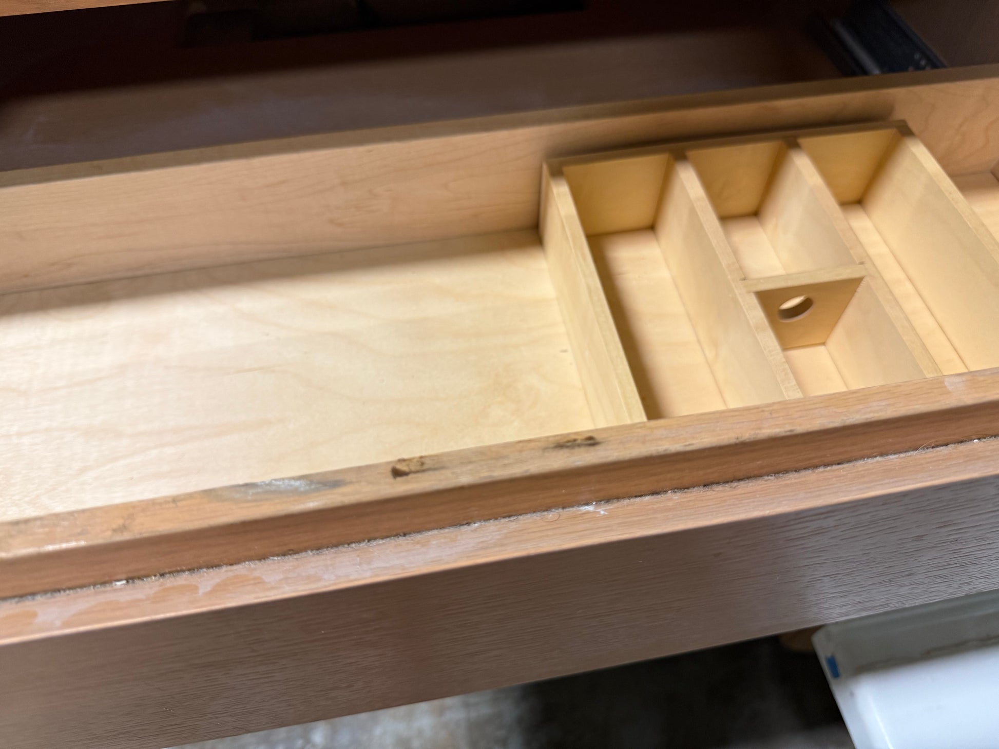 A light natural wood drawer organizer insert with multiple compartments, shown installed inside an open wooden drawer.