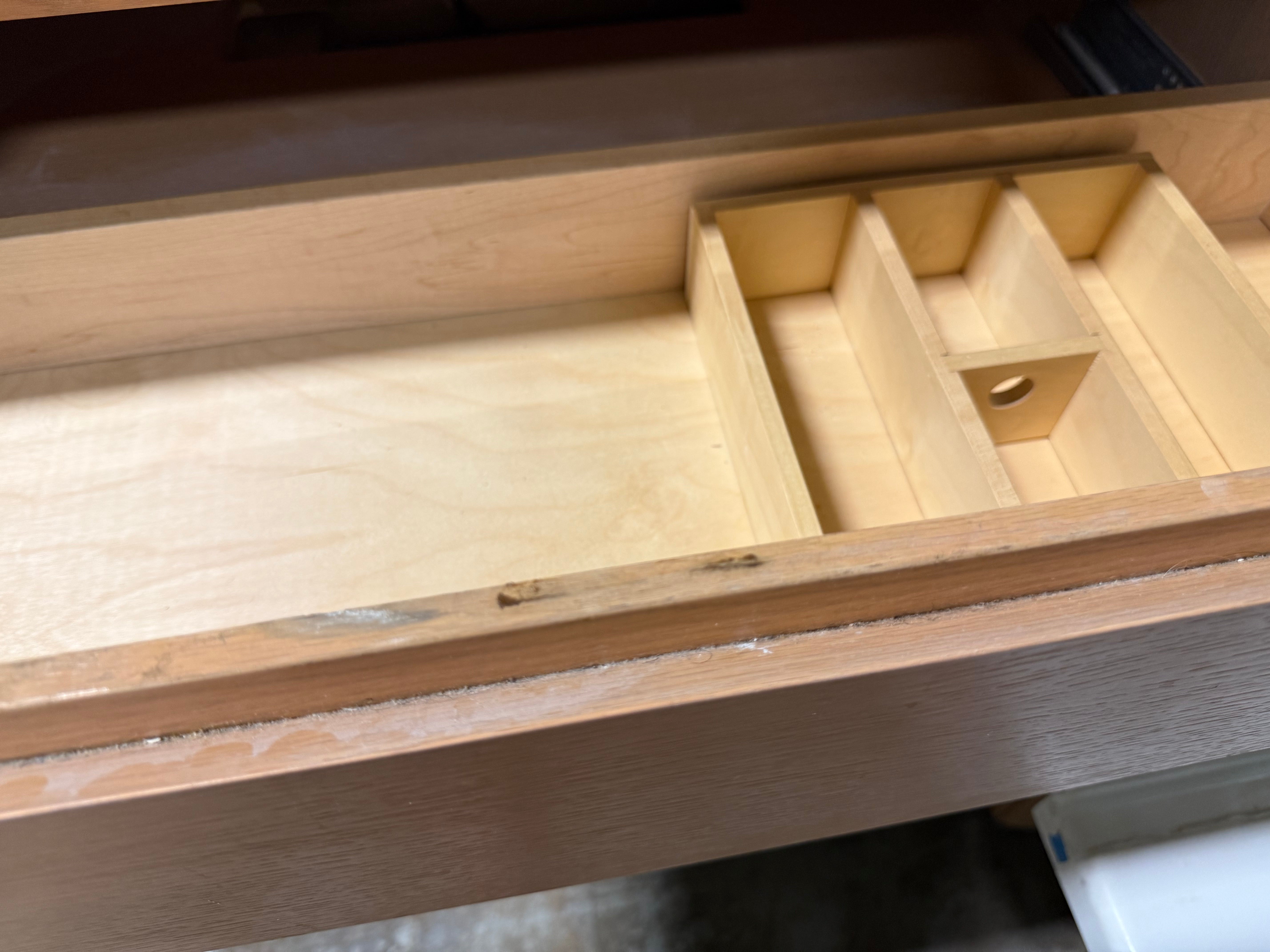A light natural wood drawer organizer insert with multiple compartments, shown installed inside an open wooden drawer.
