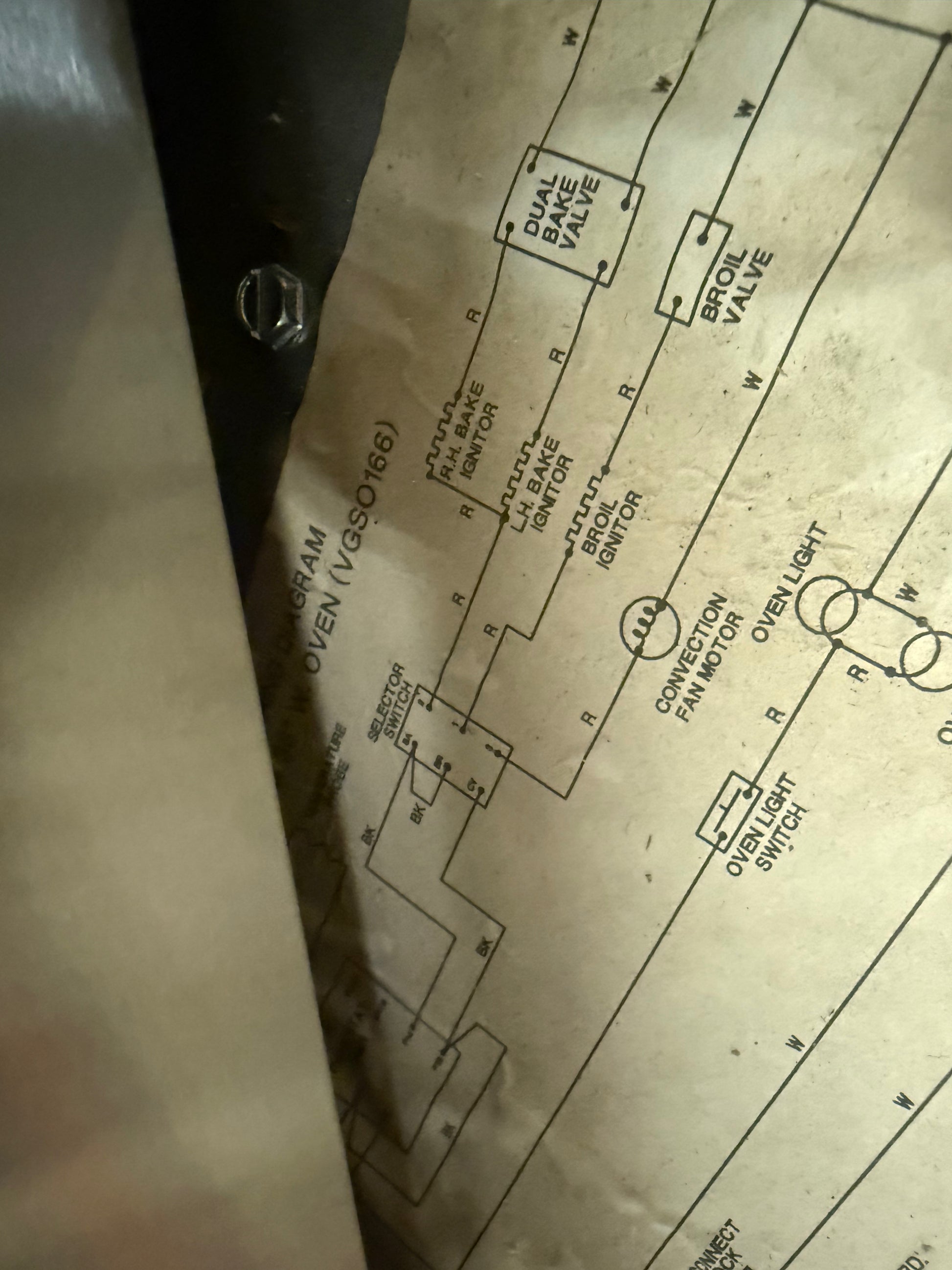 A close-up of a printed wiring diagram sheet showing automotive circuit labels such as dual valve, spark plug valve, ignition switch, and overlight switch, photographed against a dark background.