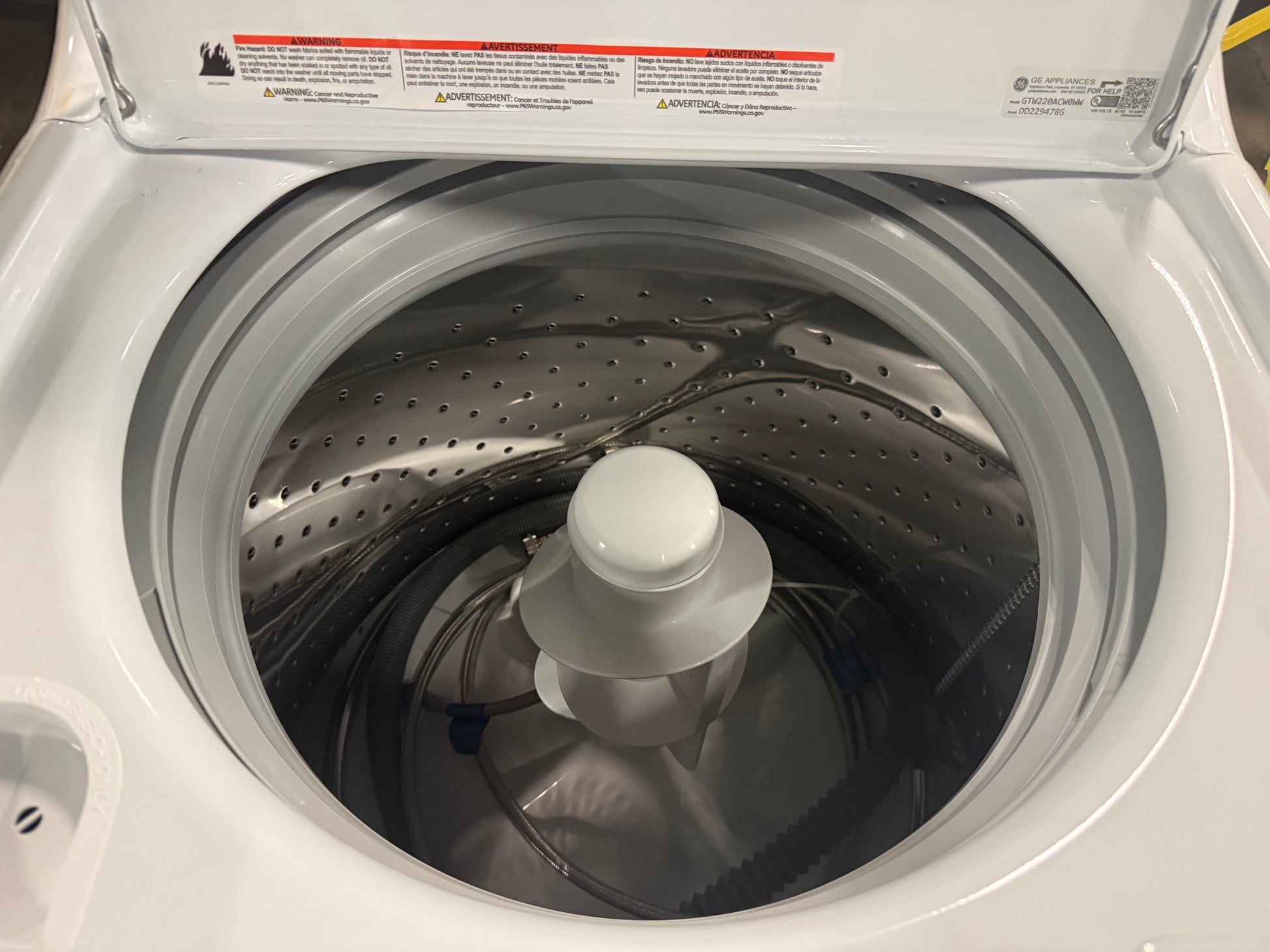 Top-loading washing machine with the lid open, showing the stainless steel drum, central agitator, and white plastic tub surround.