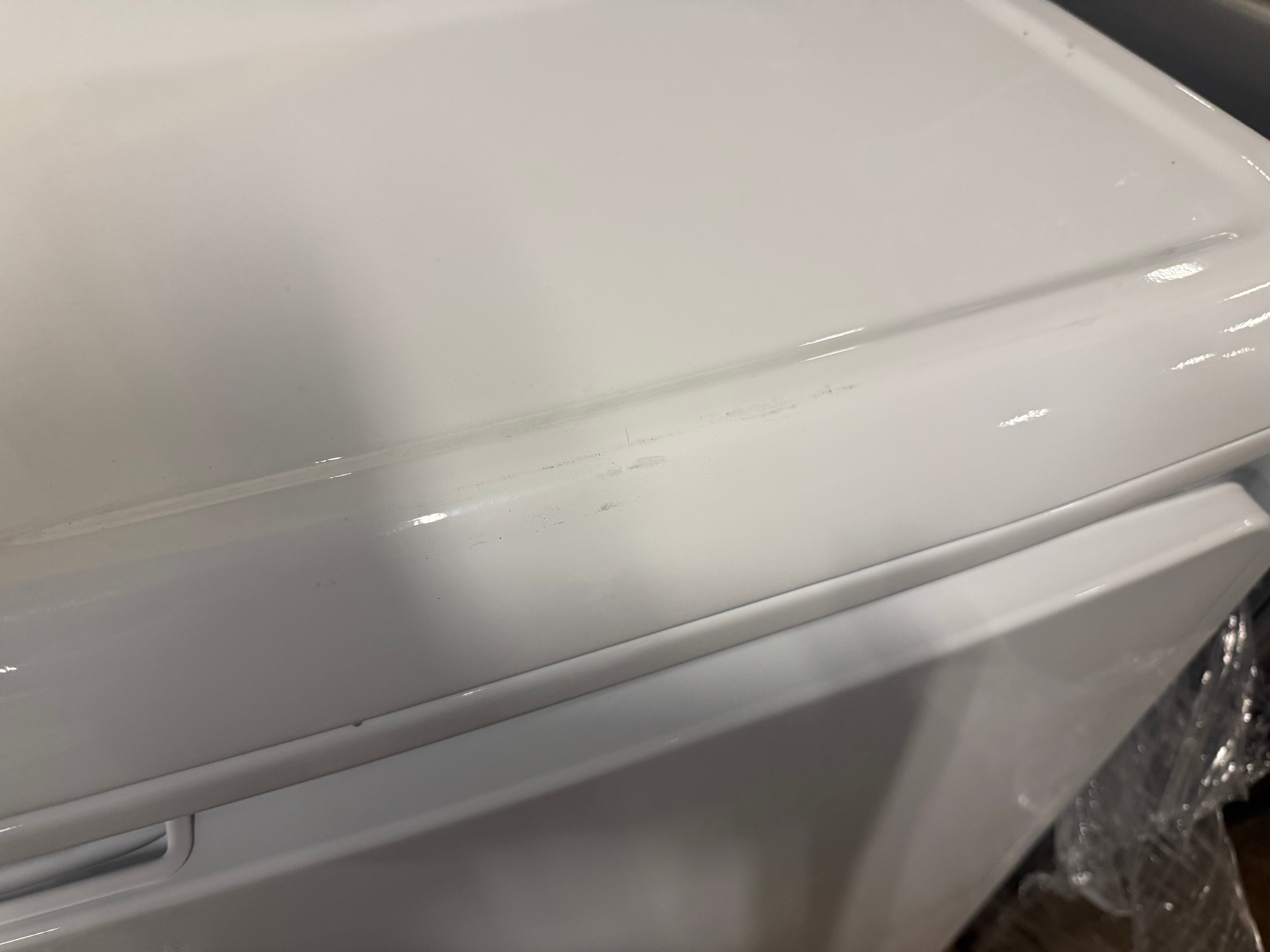 Close-up of a white appliance, likely a washing machine or dryer, showing the glossy lid edge and front panel.