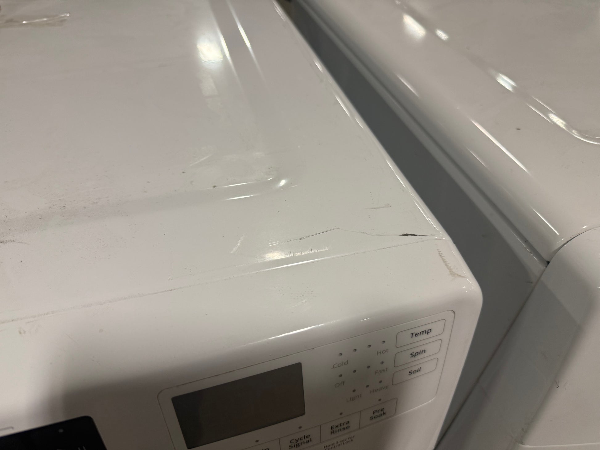 A close-up of a white appliance, likely a washing machine or dryer, showing the top control panel with a small display screen and buttons.