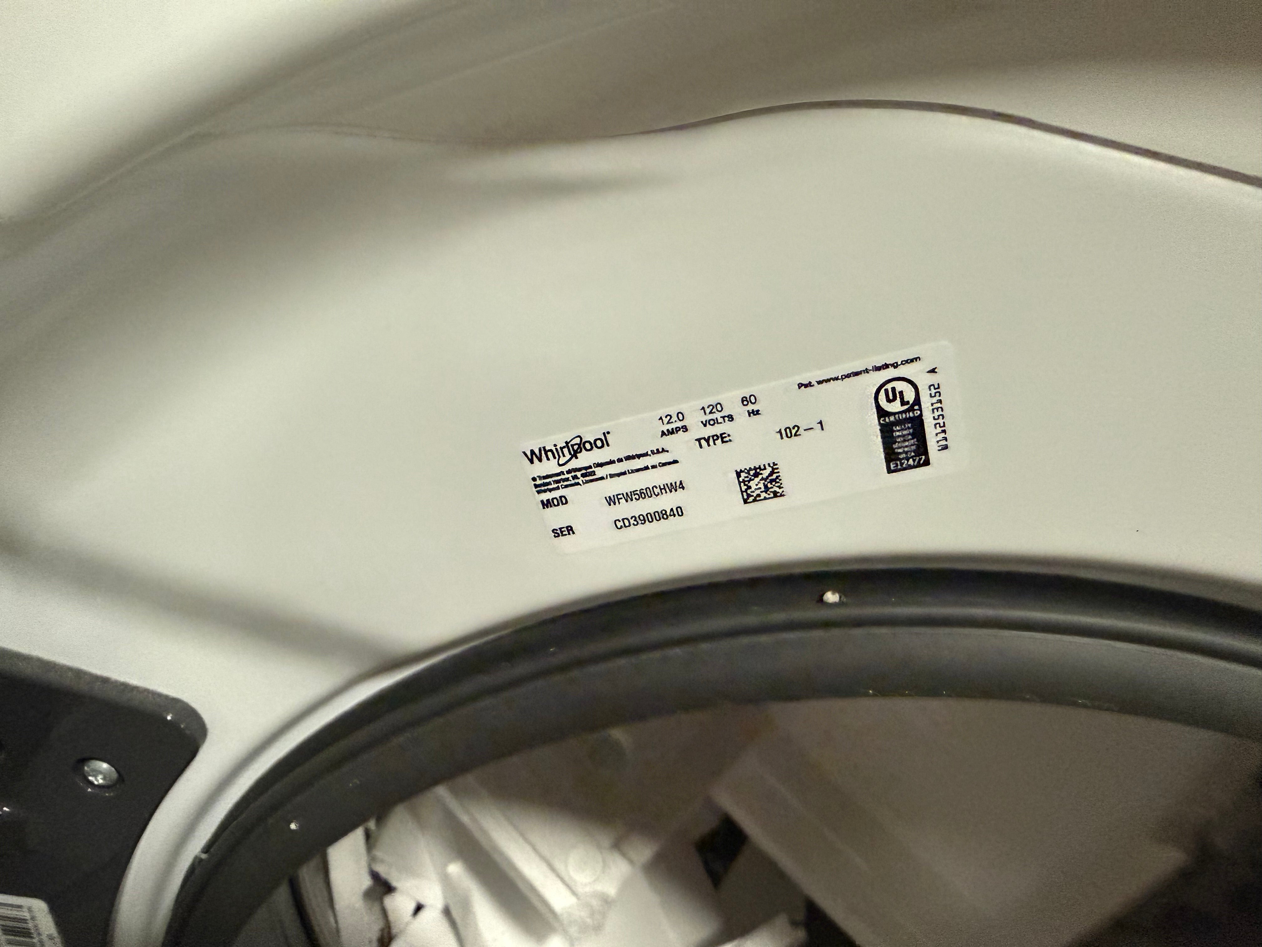 A close-up of a white appliance interior showing a Whirlpool product label on the curved inner door, with a black rubber gasket and some internal components visible below.