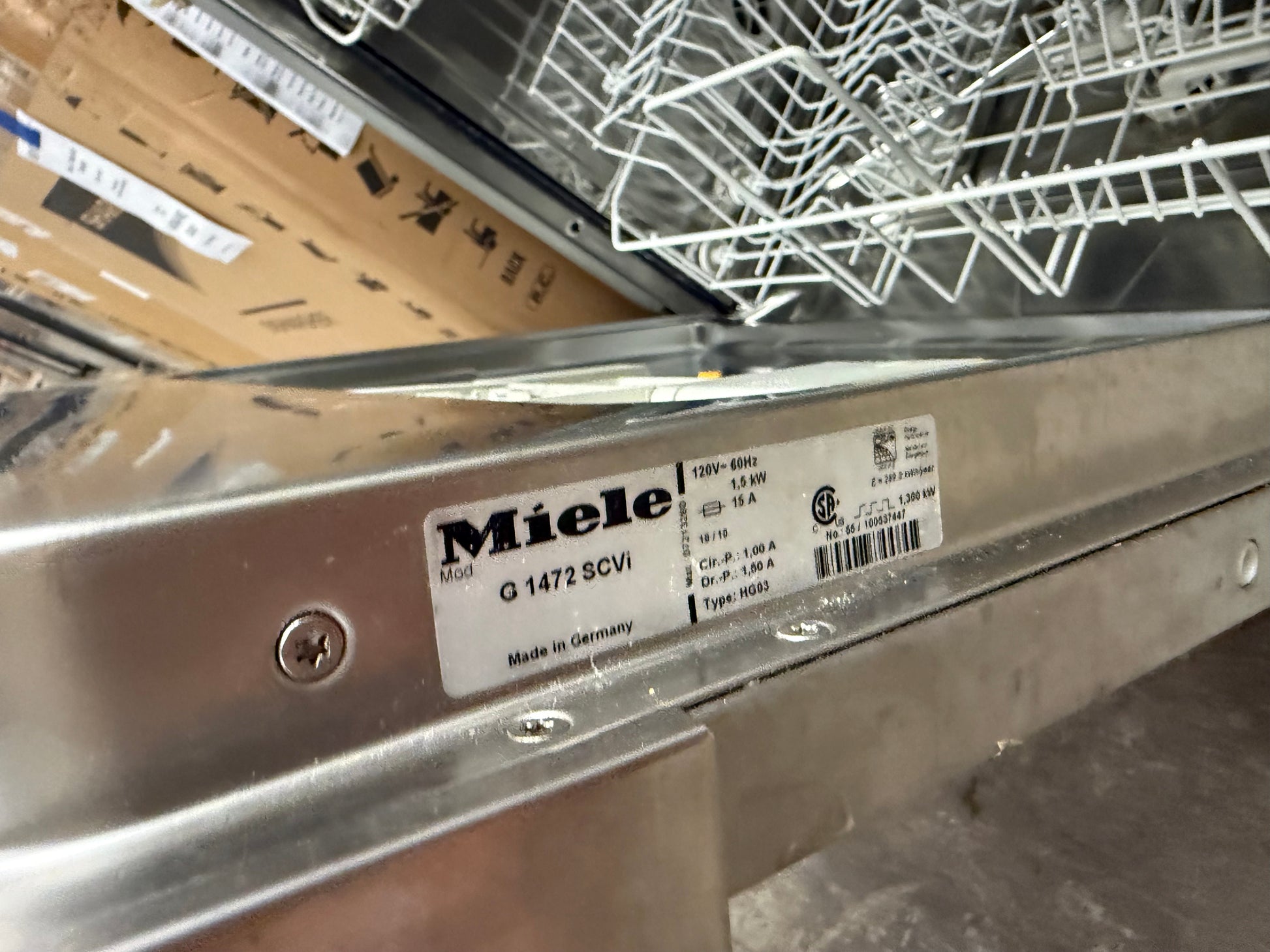 Close-up of a stainless steel dishwasher interior showing a Miele label on the inner panel and part of the white wire basket.