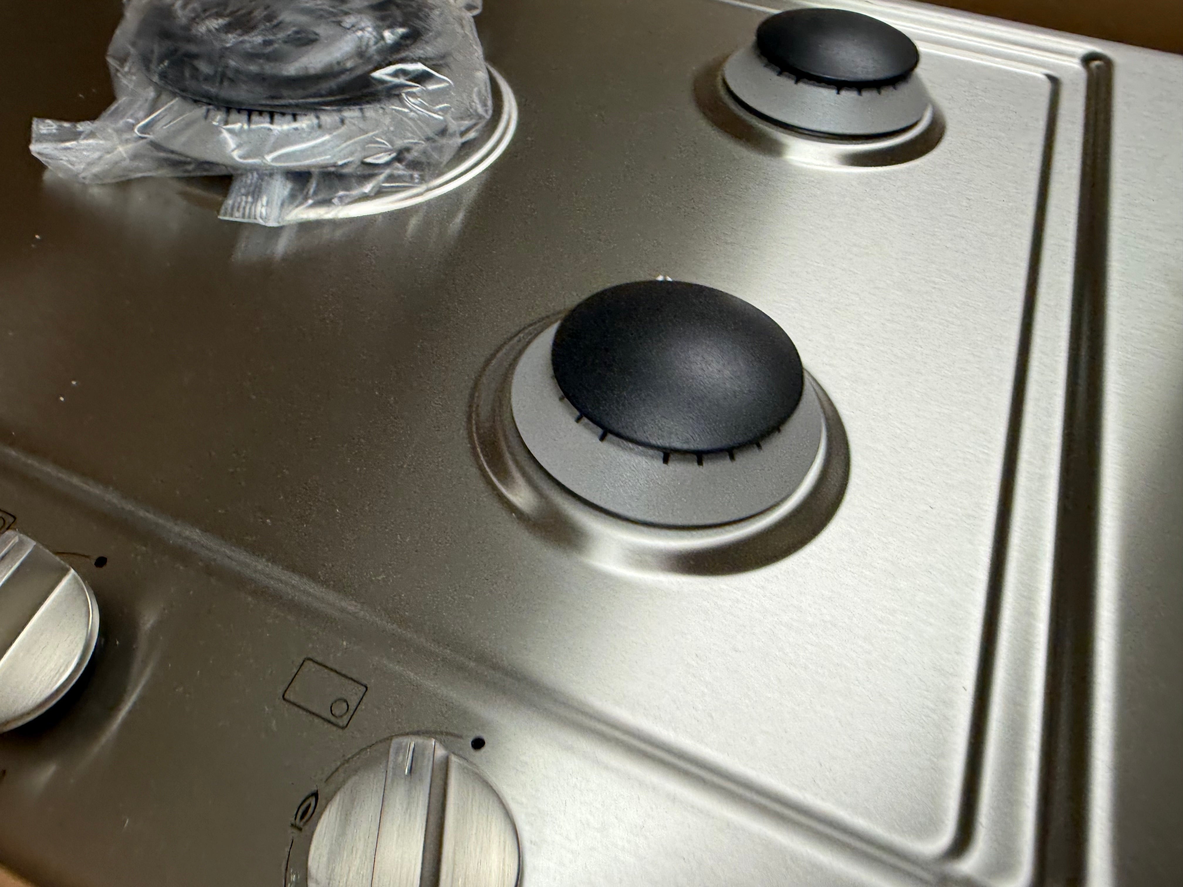 Close up of center 15300 BTU dual wok burner and metal knobs on Miele KM2032G cooktop