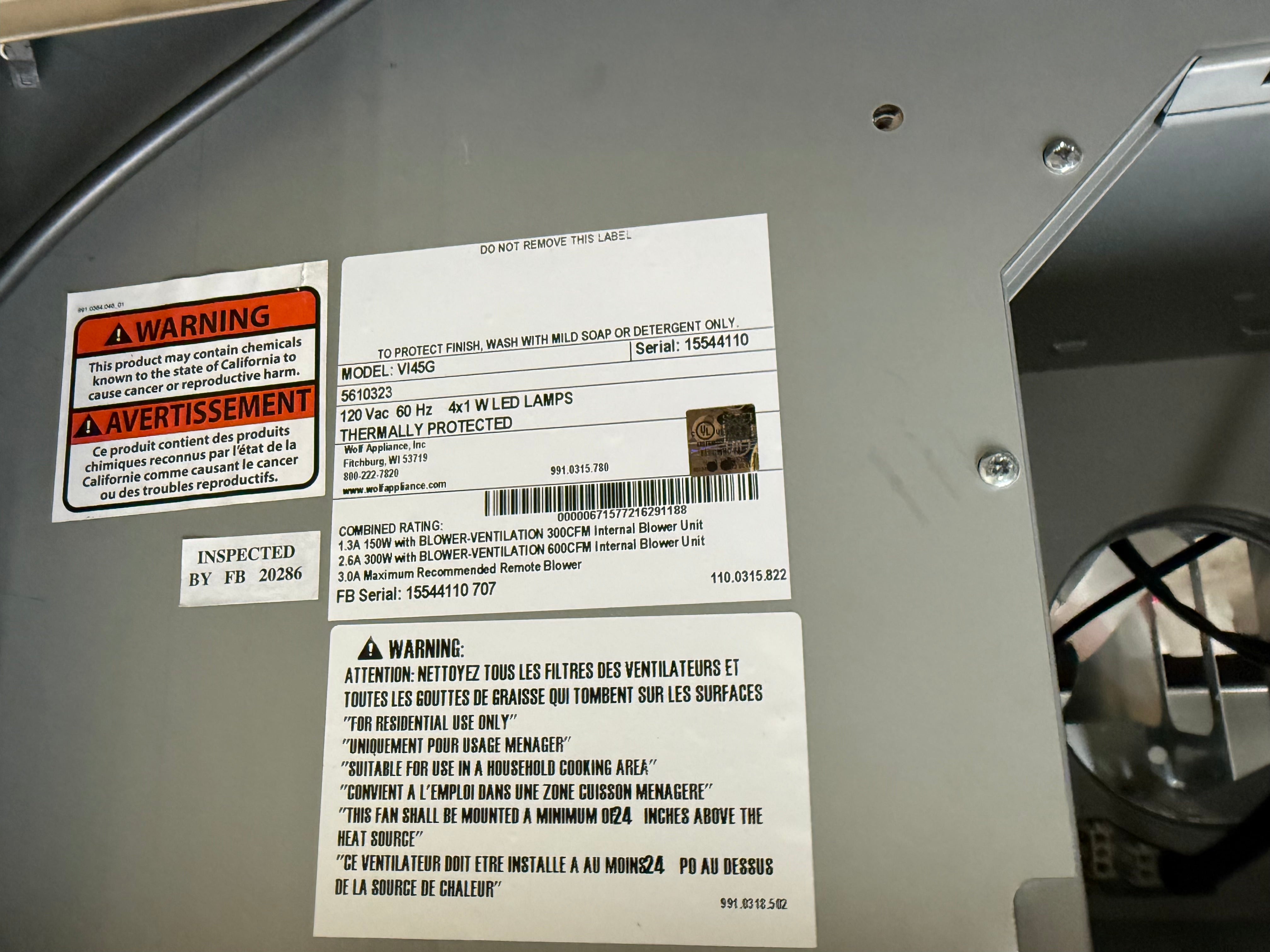 Close-up of the underside of a protective metal blower housing showing product labels, including a warning label, an inspection form, and a product info label for a 400W LED indoor blower.
