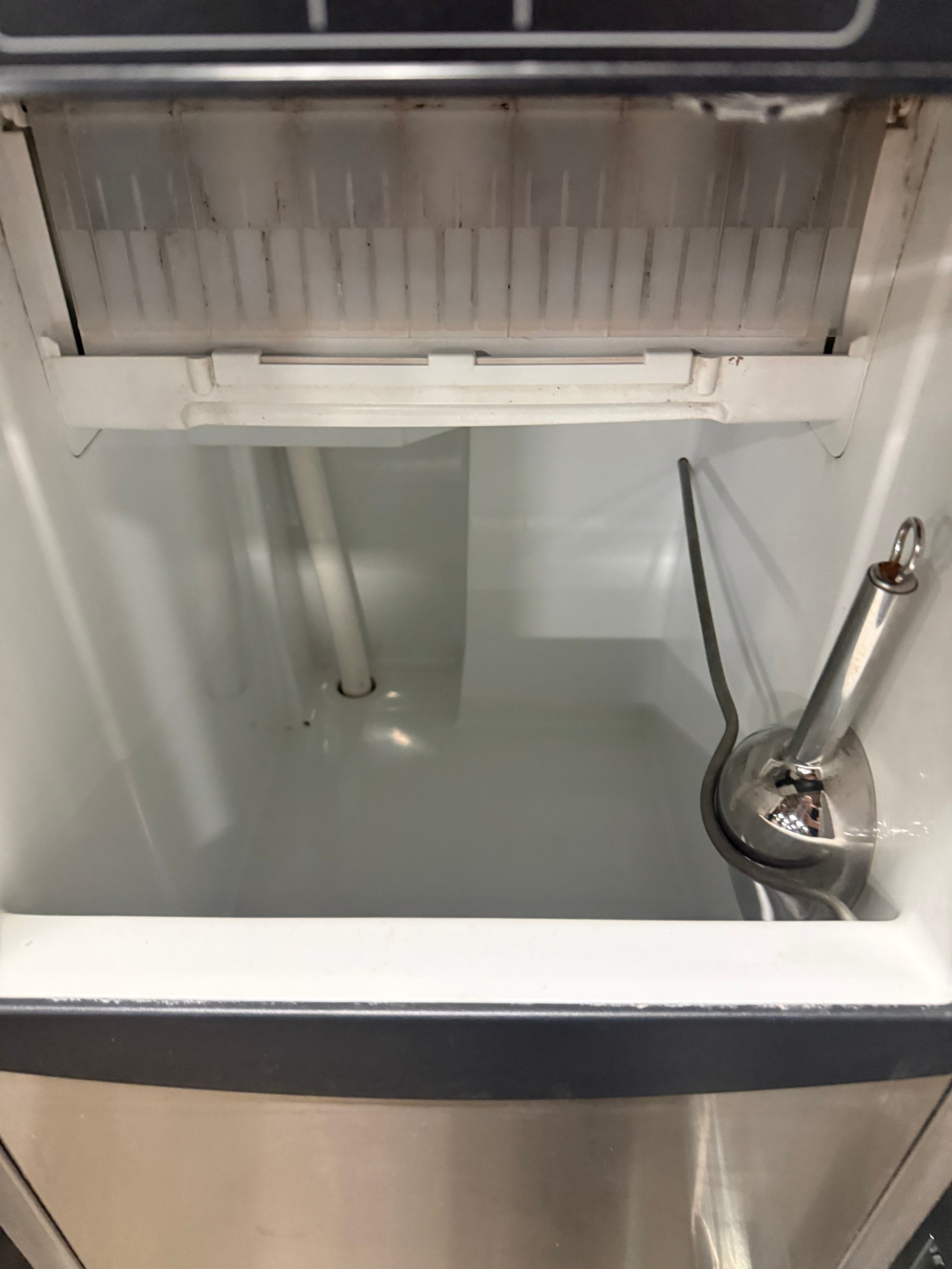 Close-up of the interior of a stainless steel and white machine, showing a metal nozzle, white plastic components, and a slotted tray at the top.