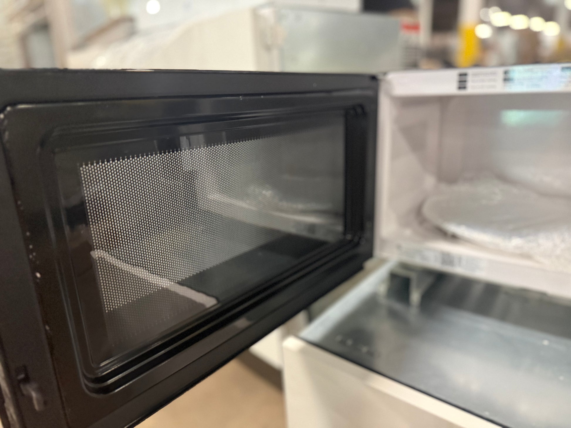 A black microwave oven with its door open, showing the glass door, mesh window, and white interior cavity.