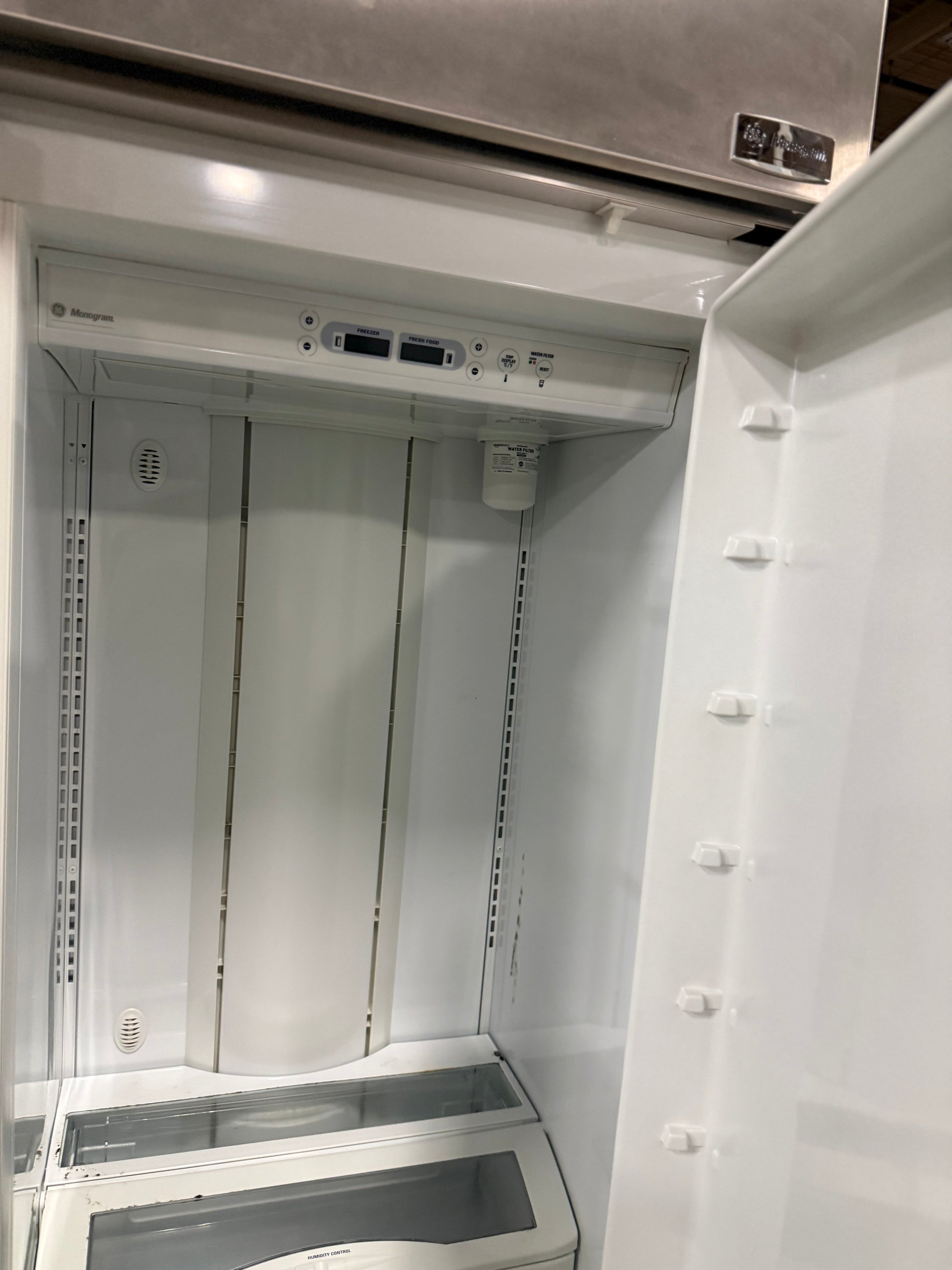 An open white refrigerator or freezer interior with a stainless steel upper appliance section visible at the top. No people or animals are present, and the photo is focused on the appliance interior rather than a styled environment.