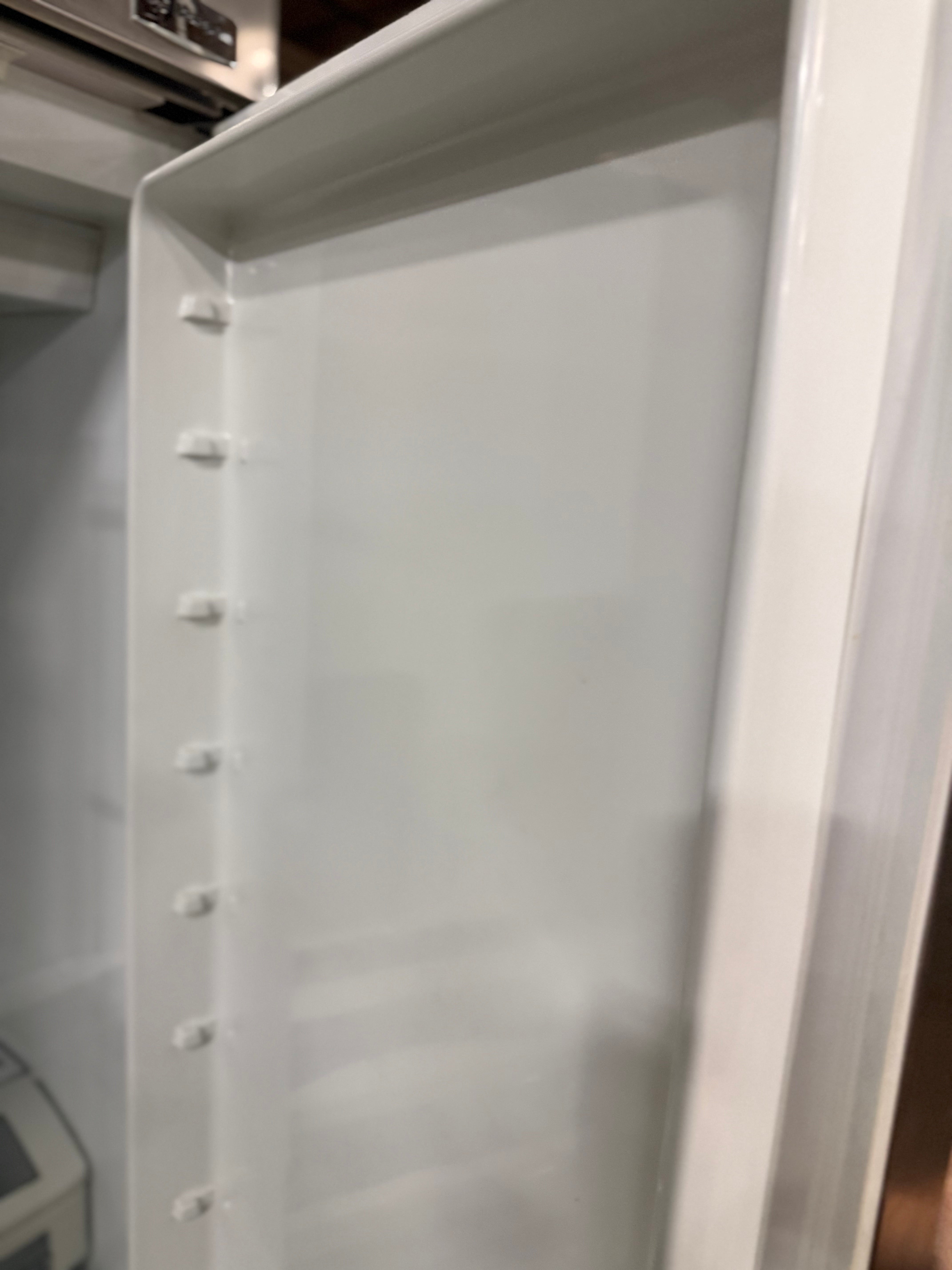An empty white refrigerator shelf with plastic mounting clips on the left side, photographed inside a refrigerator.