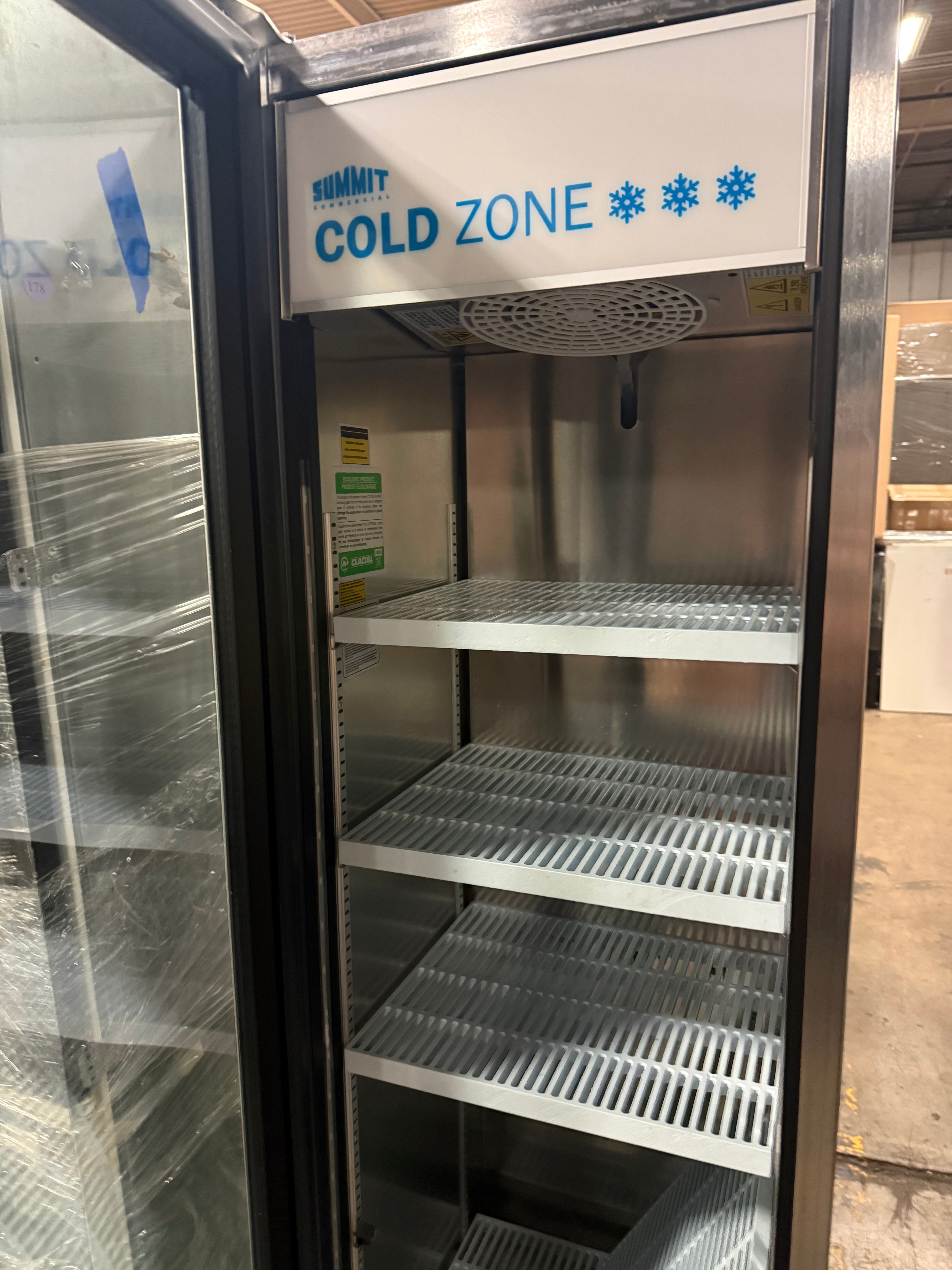 A Summit brand stainless steel commercial refrigerator with a glass door open, showing four empty metal shelves and a white top sign that reads 'COLD ZONE' with blue text and snowflake icons.