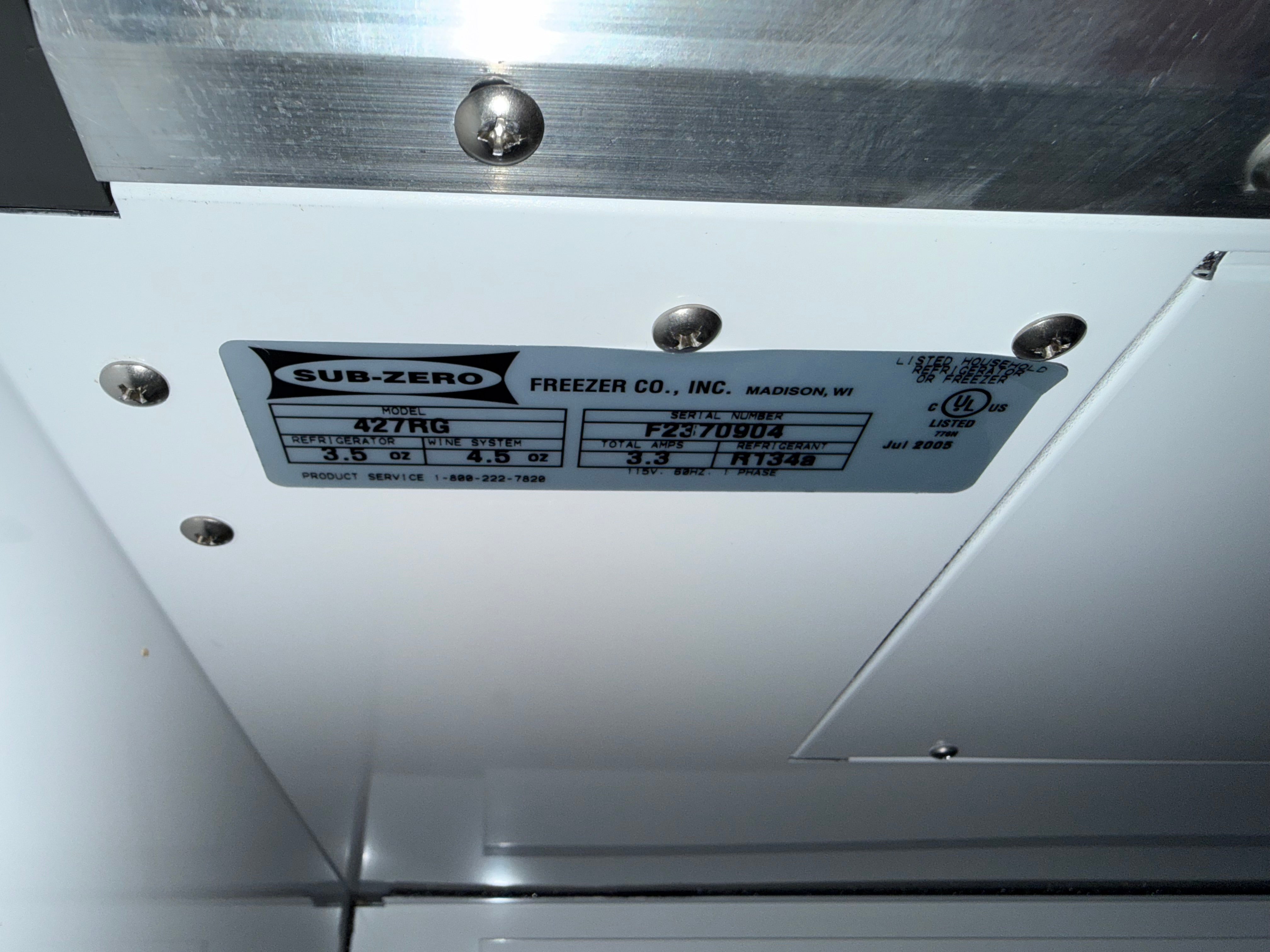 A close-up of a Sub-Zero freezer manual label attached to a white metal panel with screws, showing product specifications.