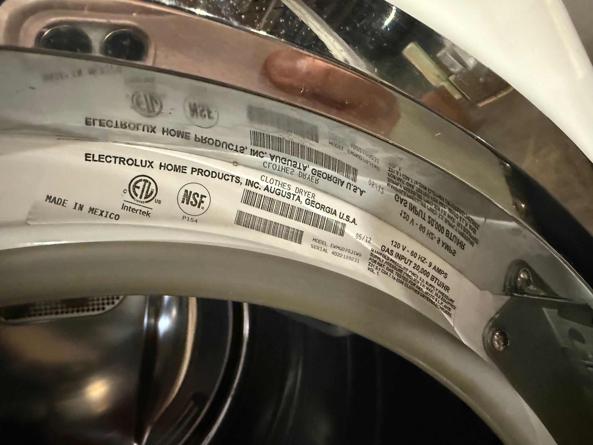 A close-up of a washing machine drum interior showing a large white product warranty label with barcodes and text, including Electrolux Home Products and NSF certification marks.