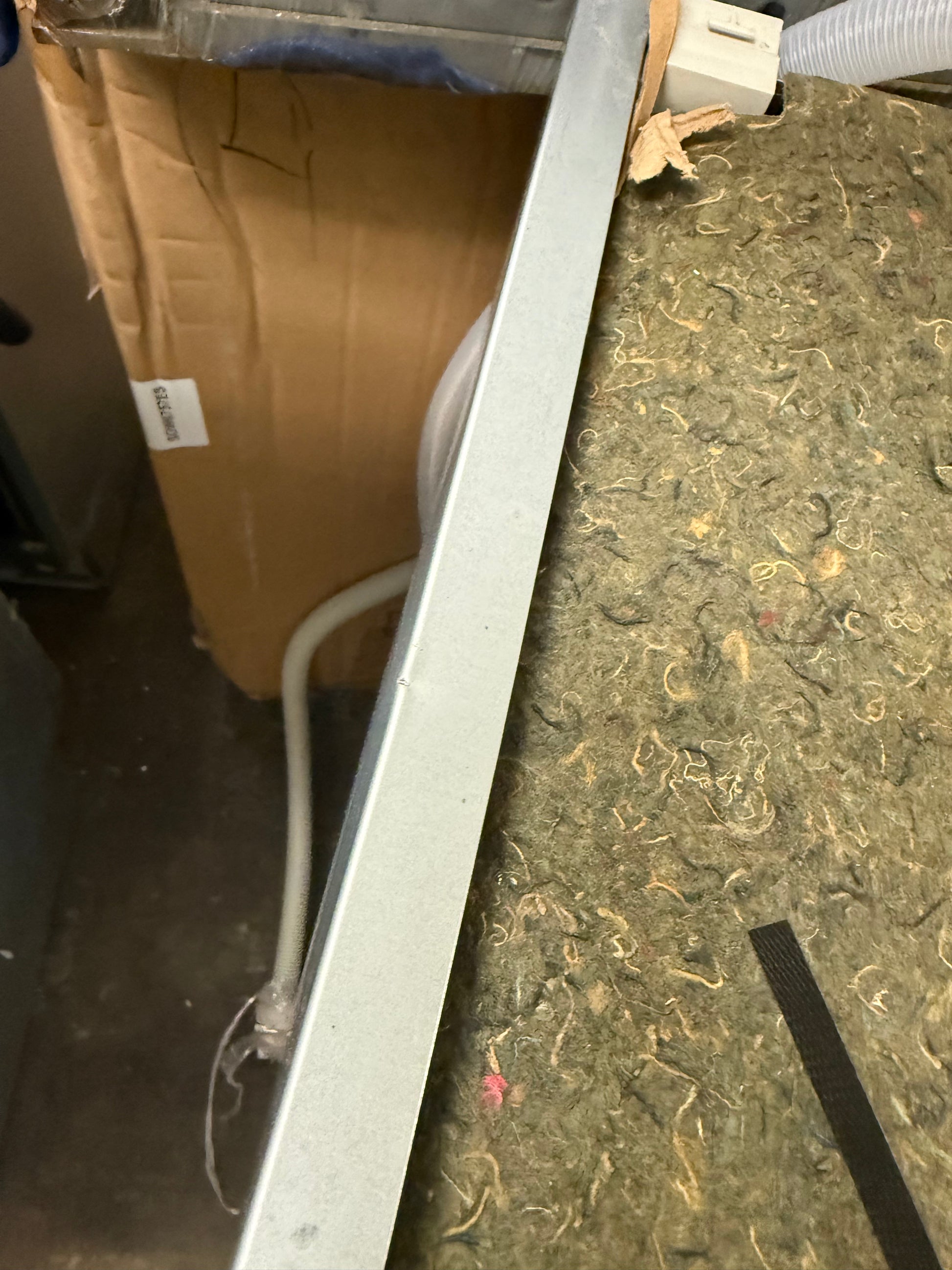 A close-up, angled view of a long, thin silver metal frame or trim piece resting on a textured green and brown carpeted floor next to a cardboard box.