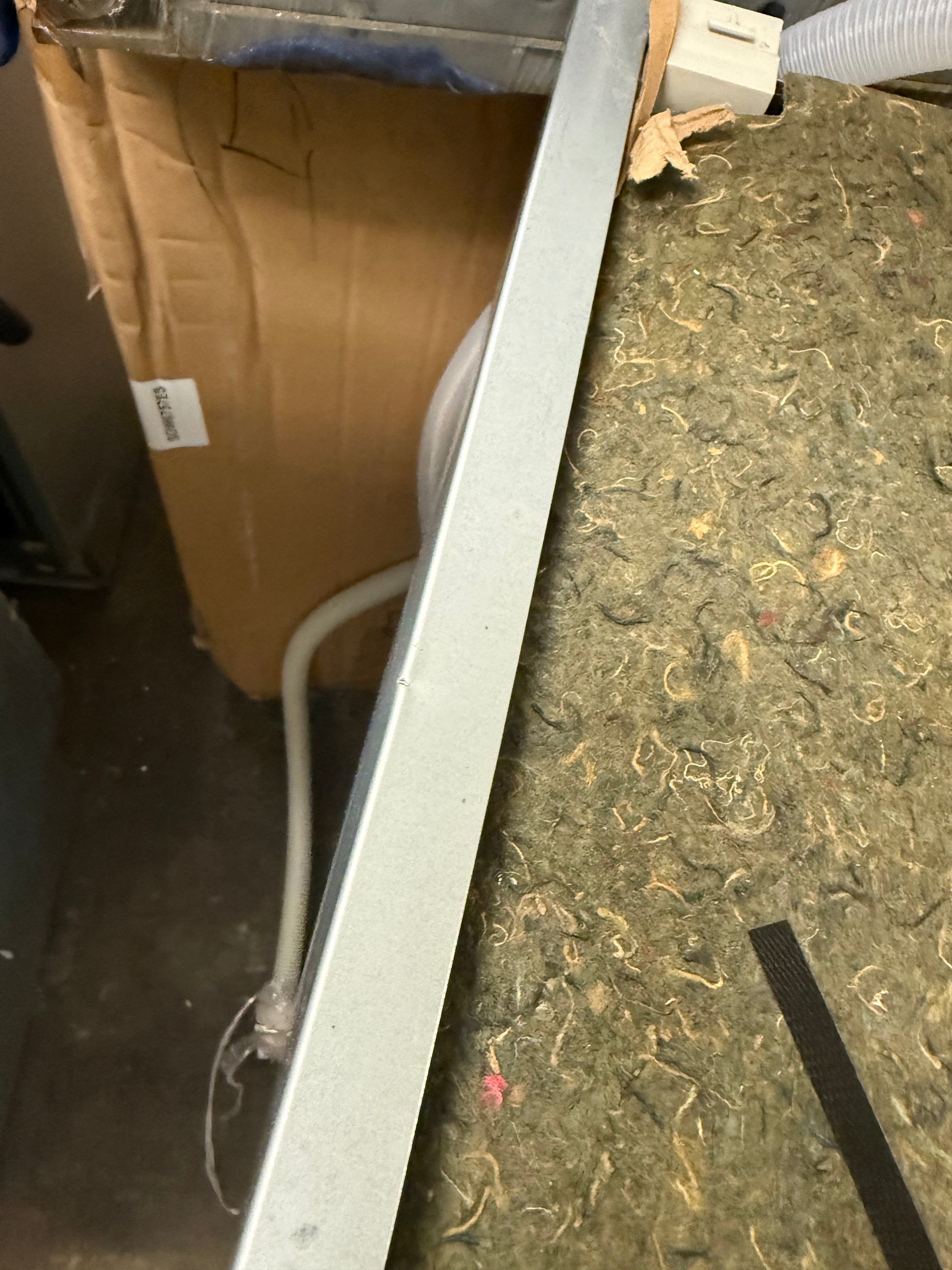 A close-up, angled view of a long, thin silver metal frame or trim piece resting on a textured green and brown carpeted floor next to a cardboard box.